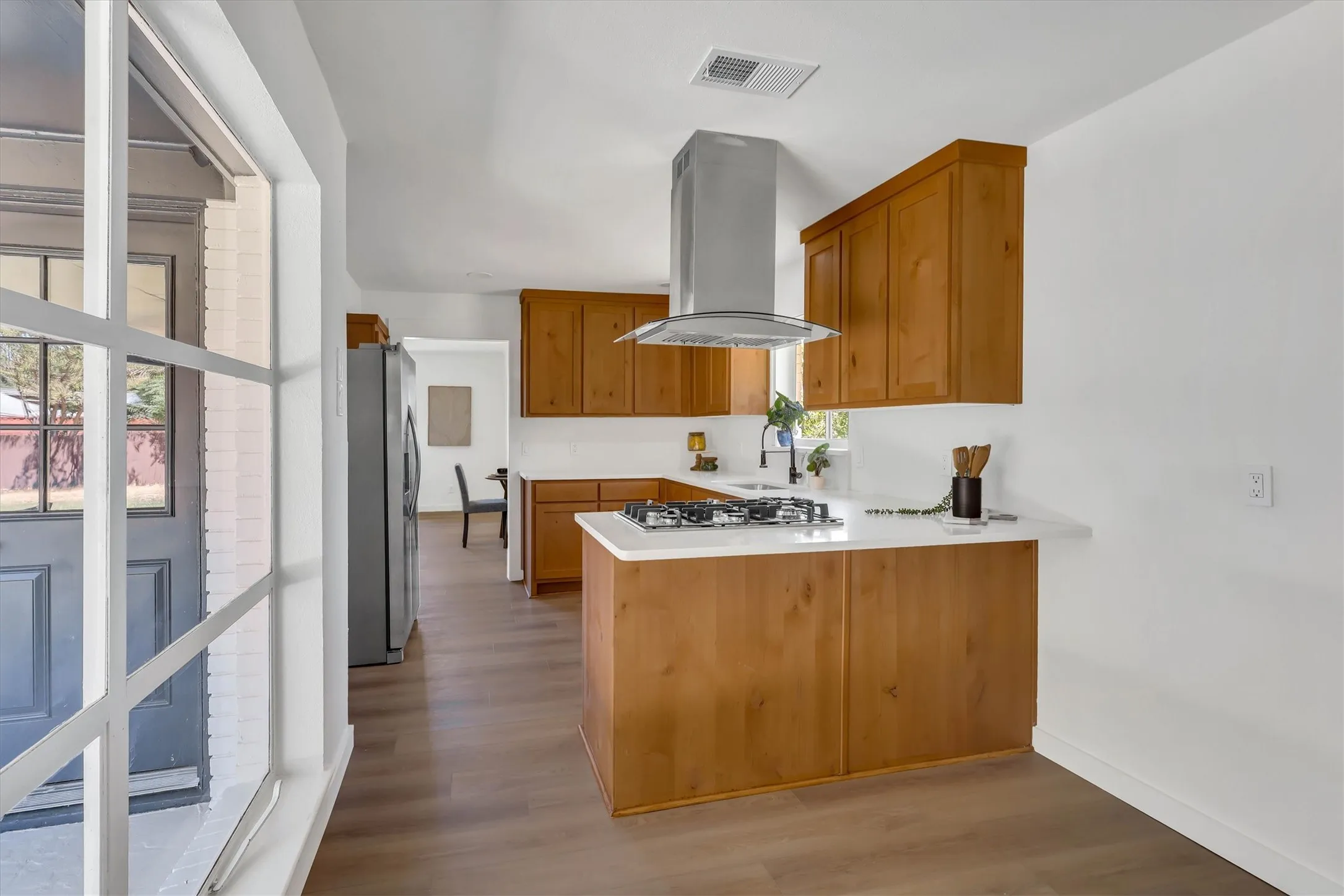Kitchen featuring wood-finish cabinetry, white countertops, a stainless steel range hood, and a gas cooktop