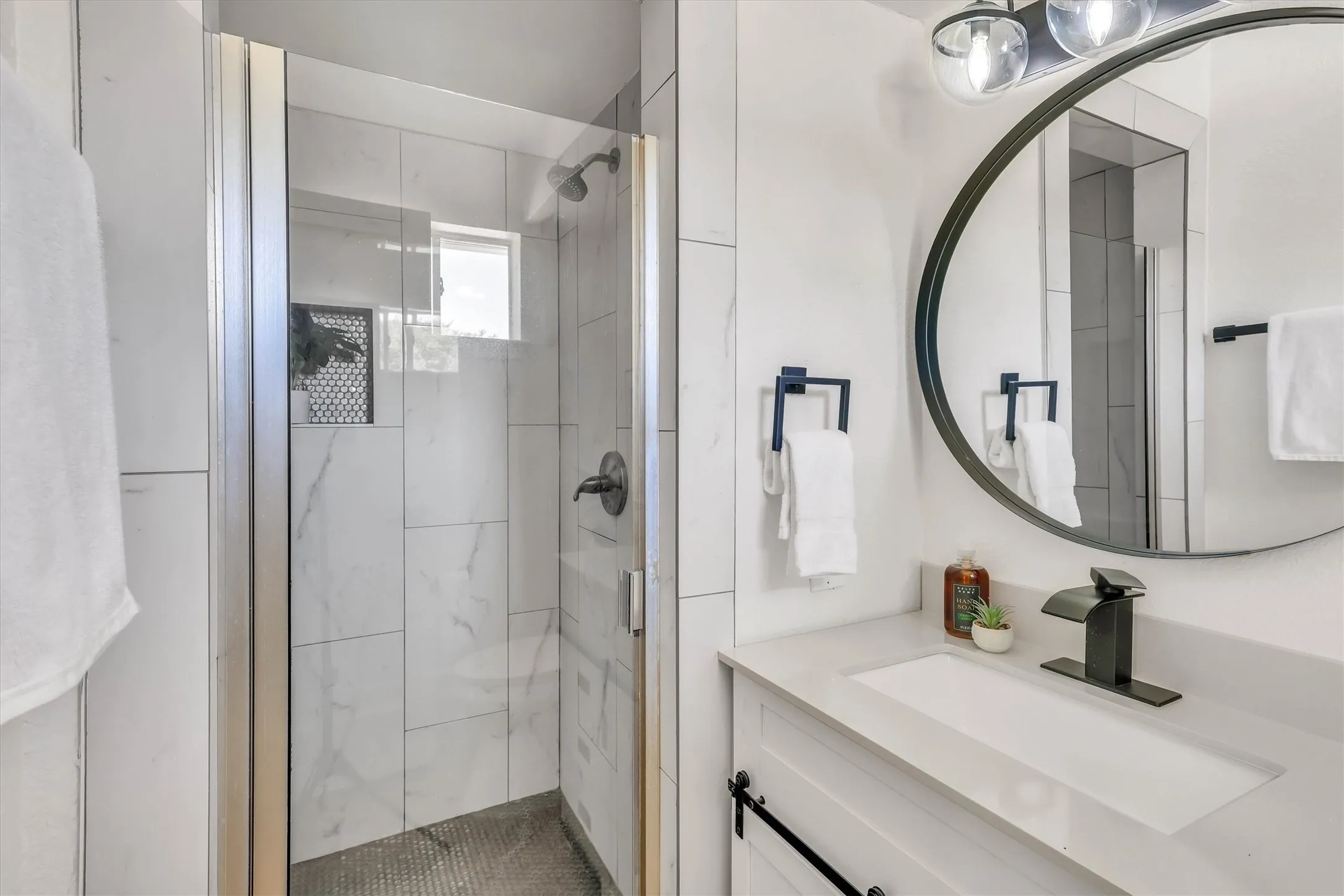 Glass-enclosed shower with white tiled walls and dark floor