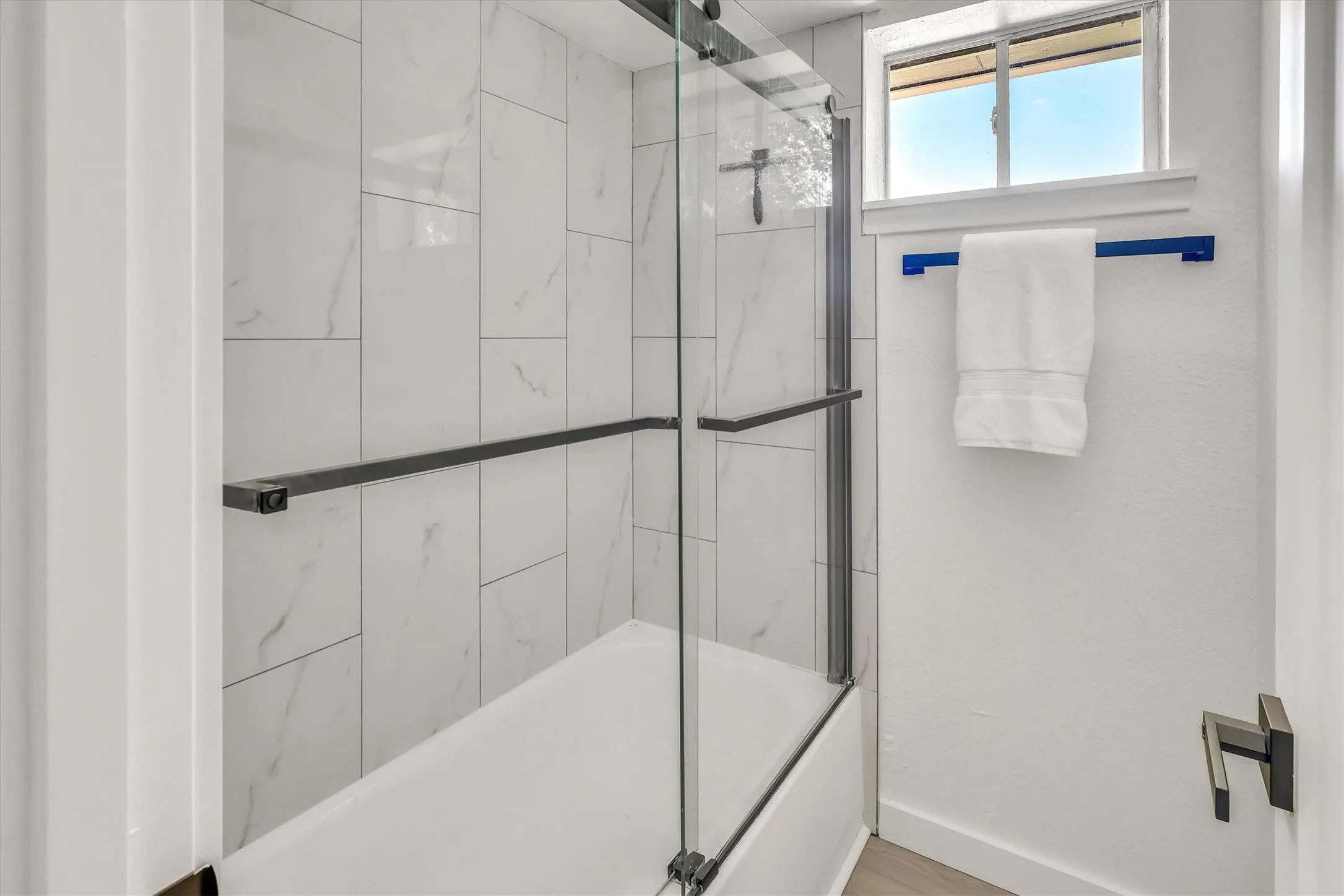 Bathtub with a glass shower enclosure, white tiled surround, and matte black hardware