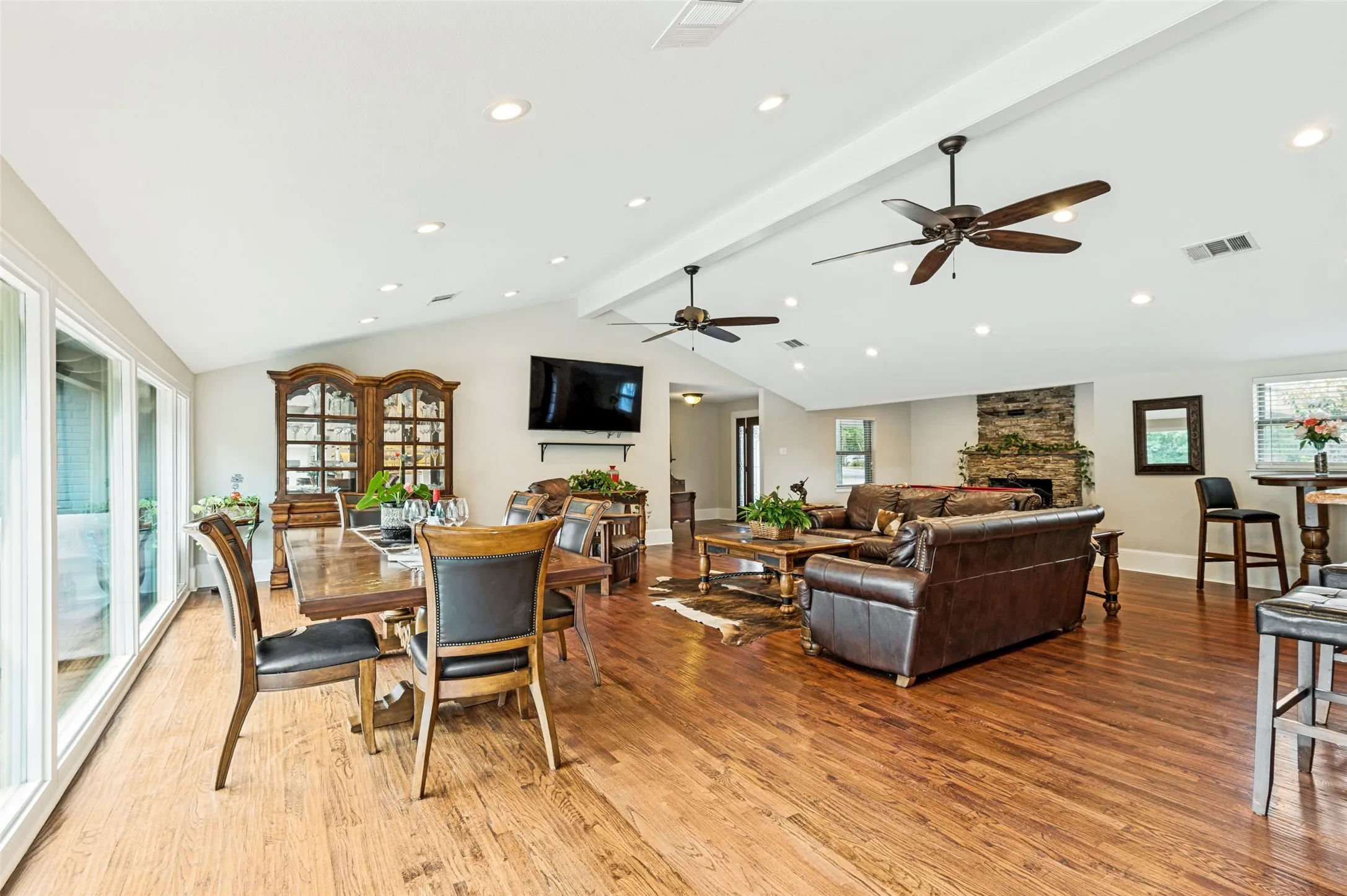 Vaulted ceilings with recessed lighting and ceiling fans, wood-finish flooring, and a stone-clad fireplace