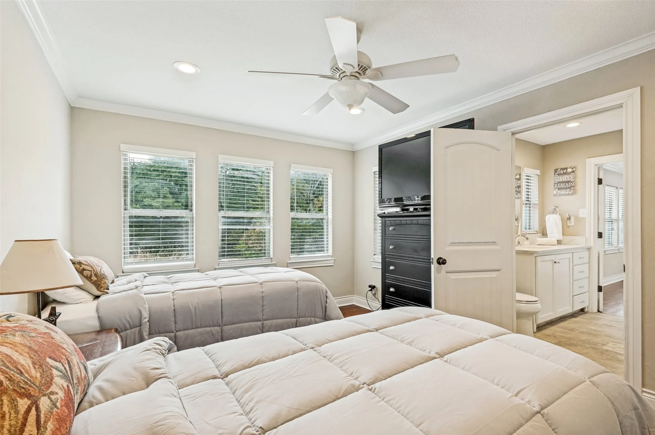 Recessed ceiling lighting, crown molding, three windows with blinds, a ceiling fan, and access to a full bathroom with a single vanity