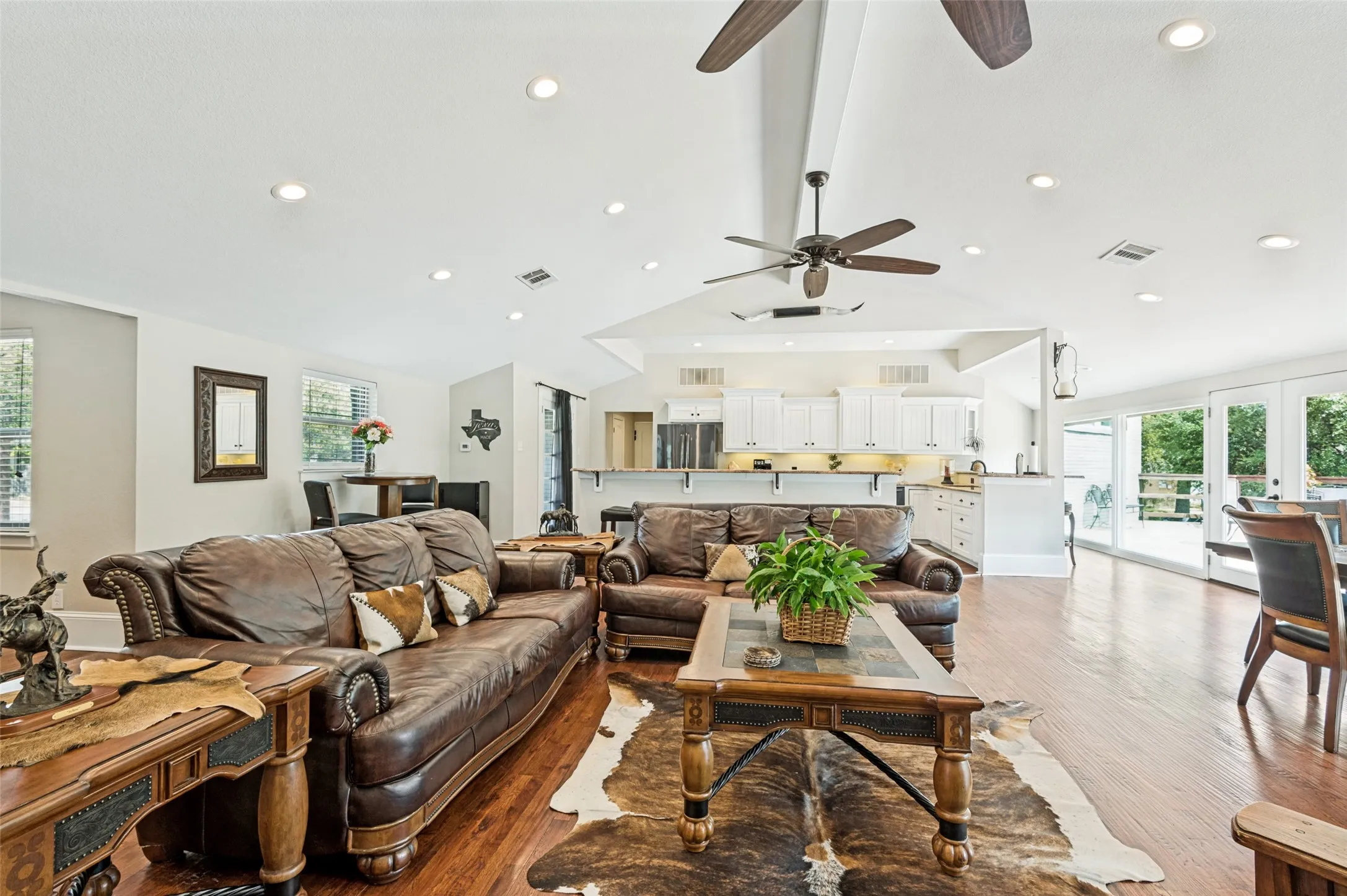 Vaulted ceilings, recessed lighting, wood-finish flooring, white kitchen cabinetry, and patio access