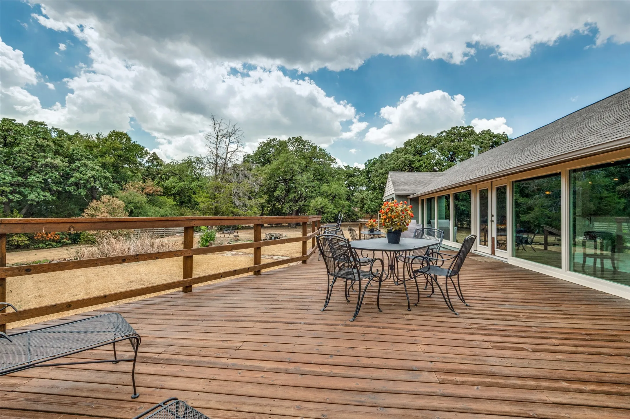 Expansive outdoor deck with natural wood finish, a durable wood railing, and a seamless connection to the interior via multiple large pane windows and a glass-paneled door