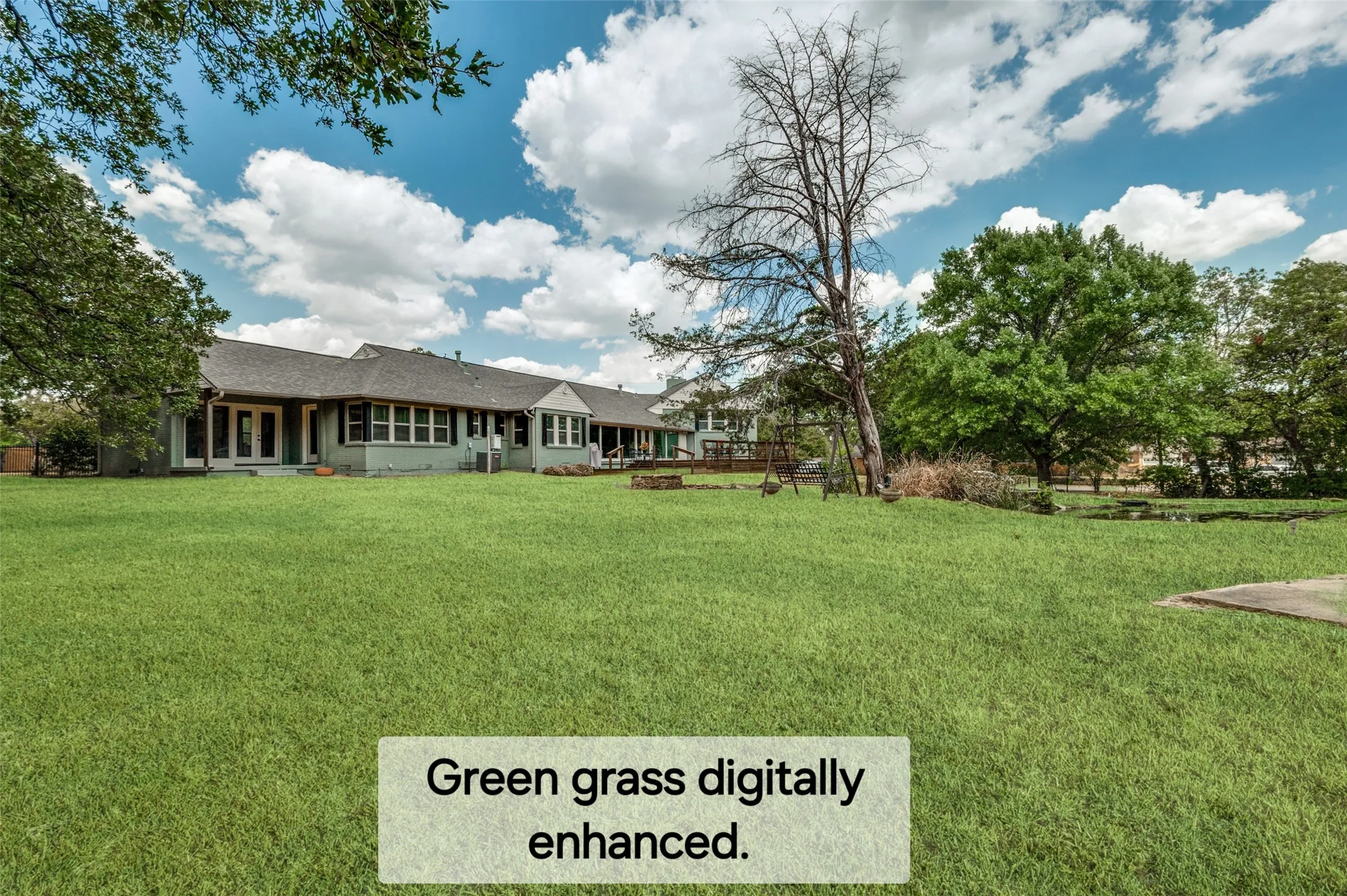 Expansive green lawn with mature trees and a single-story residence featuring multiple windows and a covered patio area