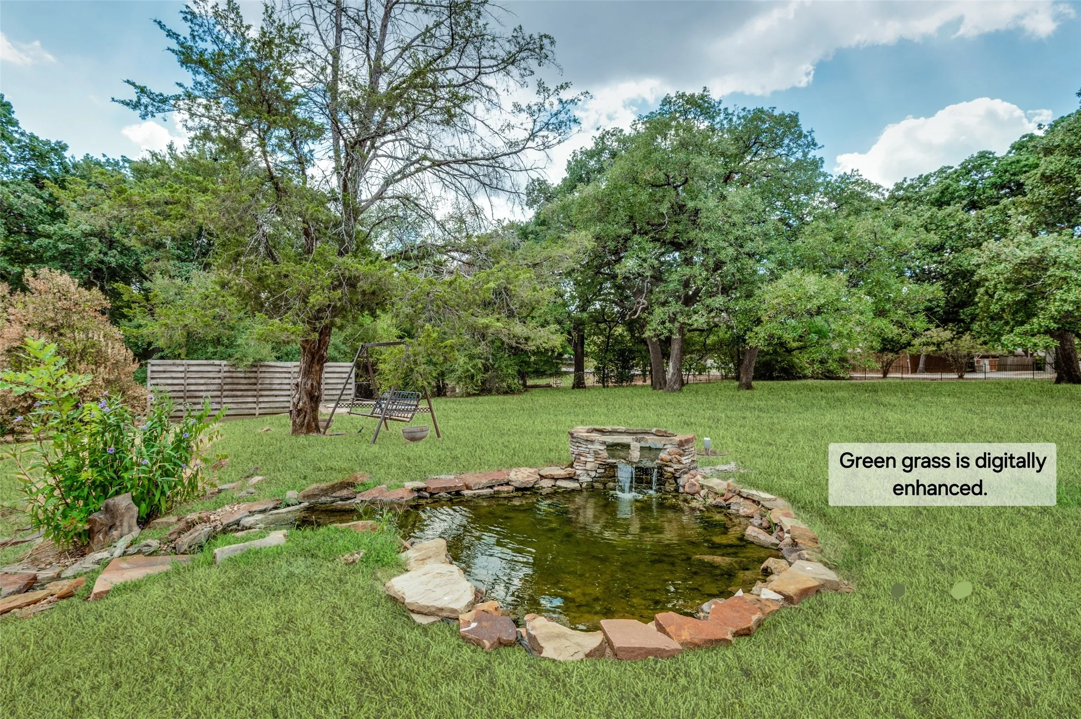 Expansive backyard featuring a stone-lined pond with a waterfall feature, mature trees, and a wood privacy fence