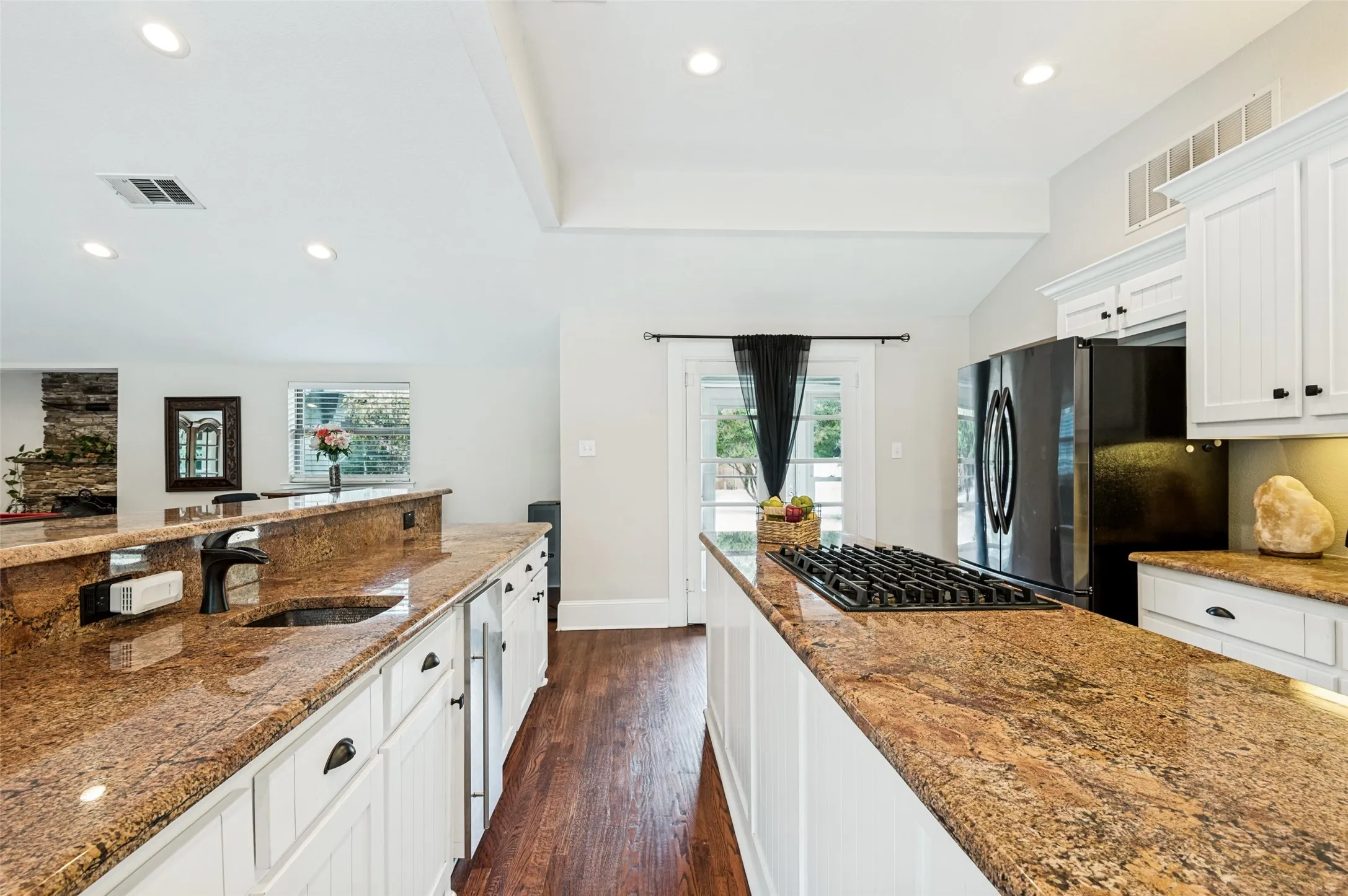 Kitchen featuring expansive stone countertops, white cabinetry with dark hardware, a built-in gas cooktop, a stainless steel sink with a dark faucet, and wood-finish flooring
