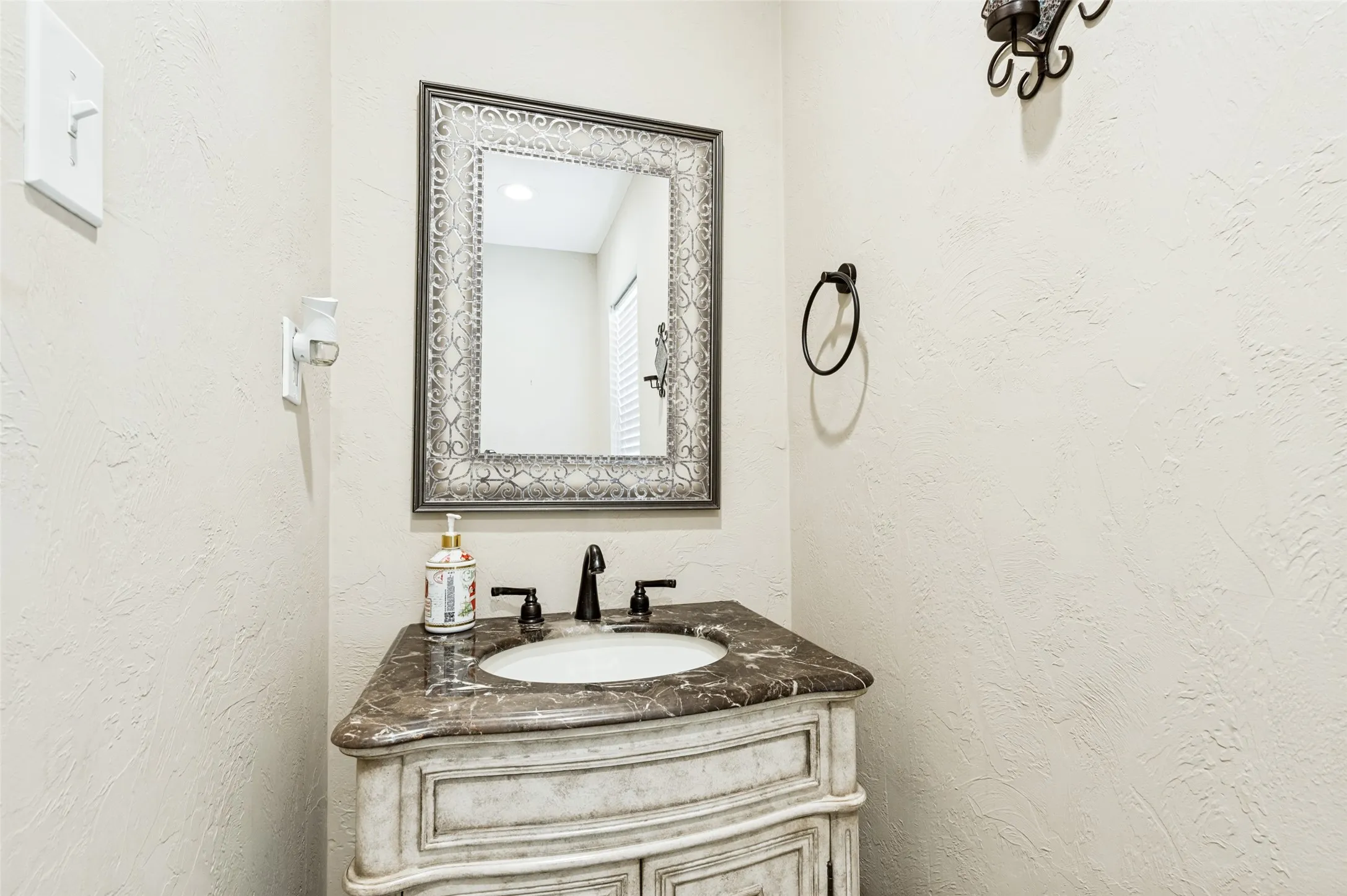 Half bath with distressed white vanity with curved cabinet doors, dark countertop, and an undermount sink