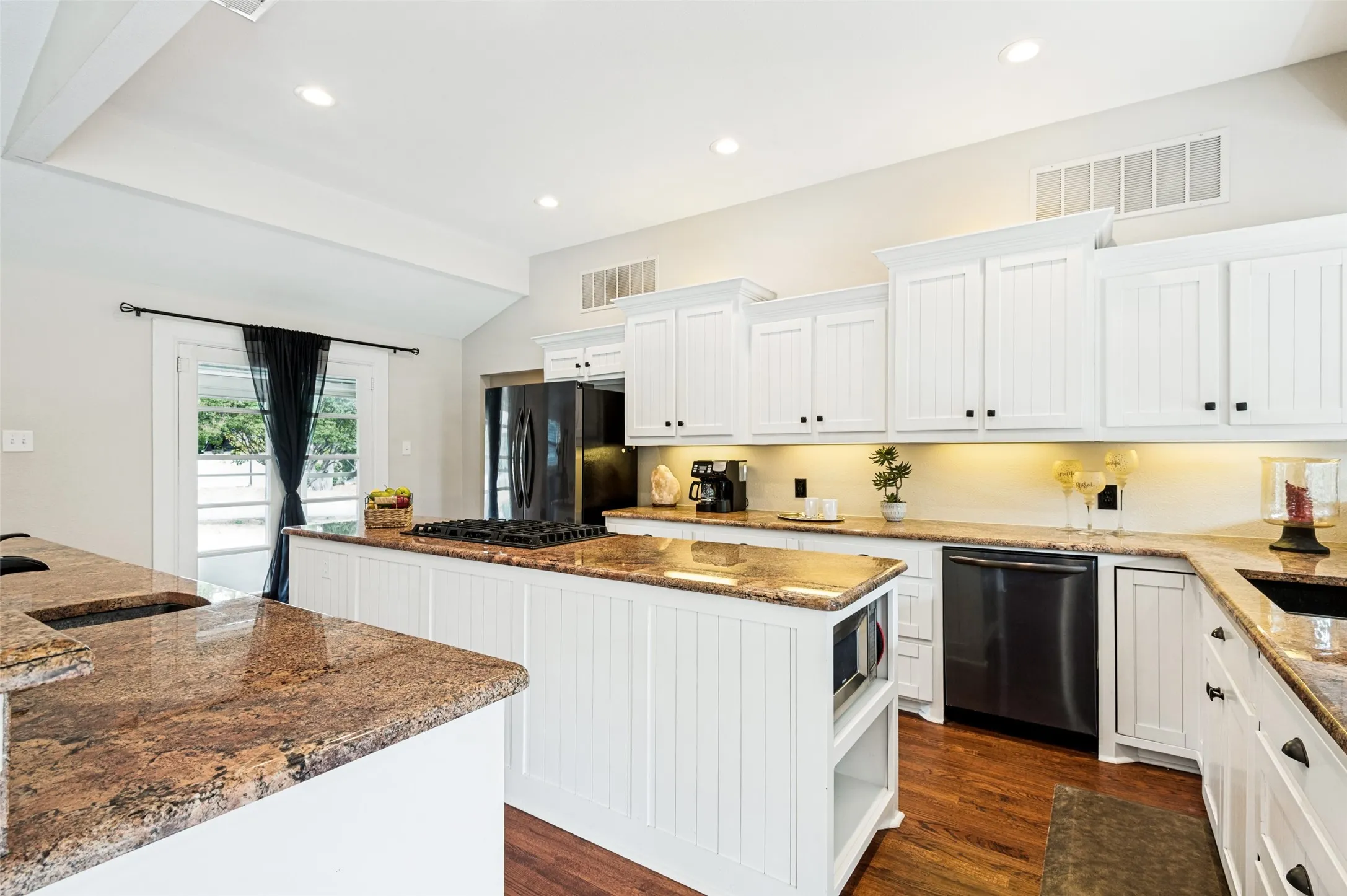 White cabinetry with black hardware, granite countertops, recessed lighting, wood-finish flooring, and a built-in microwave