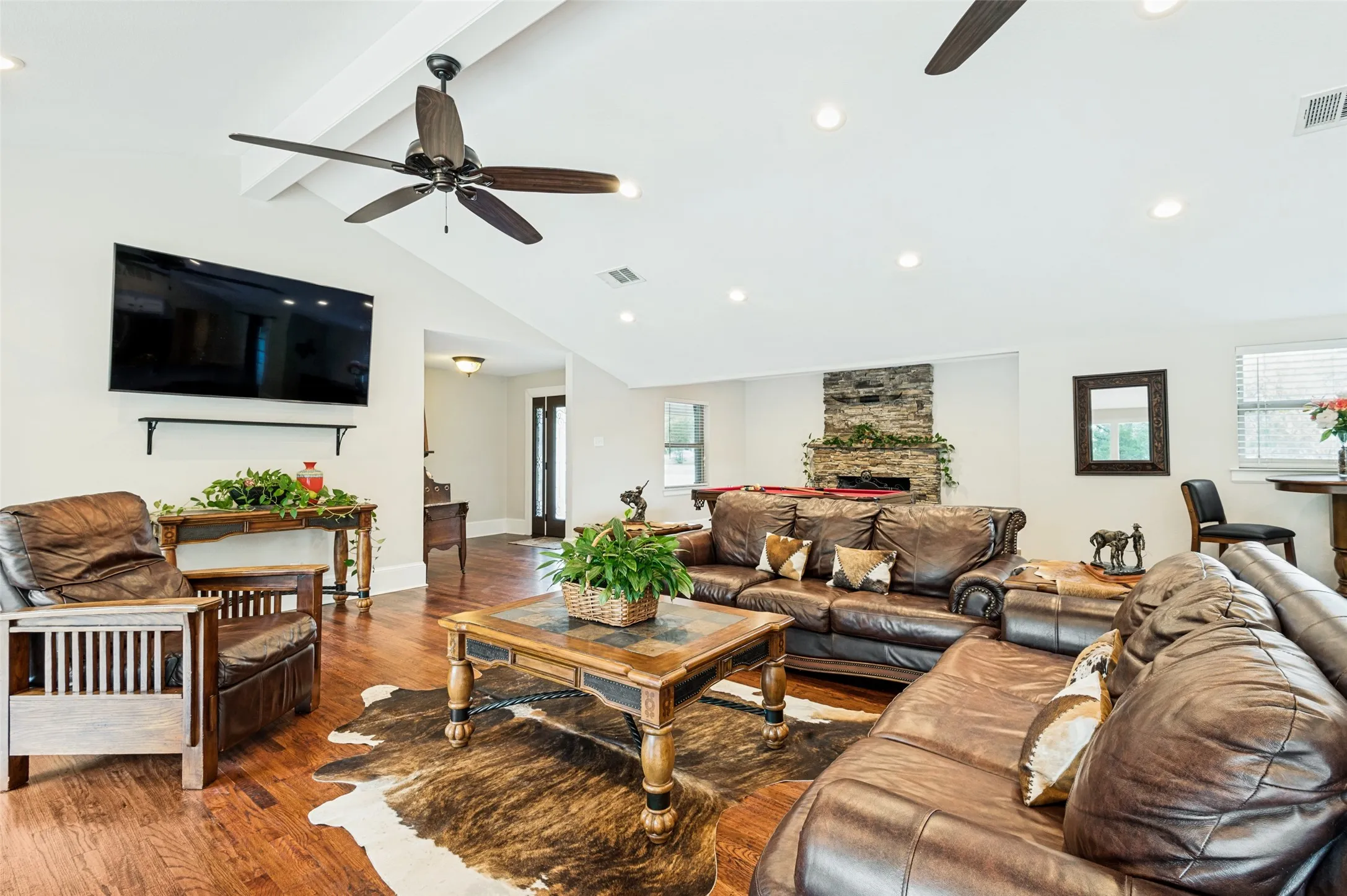 Vaulted ceiling with exposed beams, wood-finish flooring, stone-clad fireplace, recessed lighting, and ceiling fans
