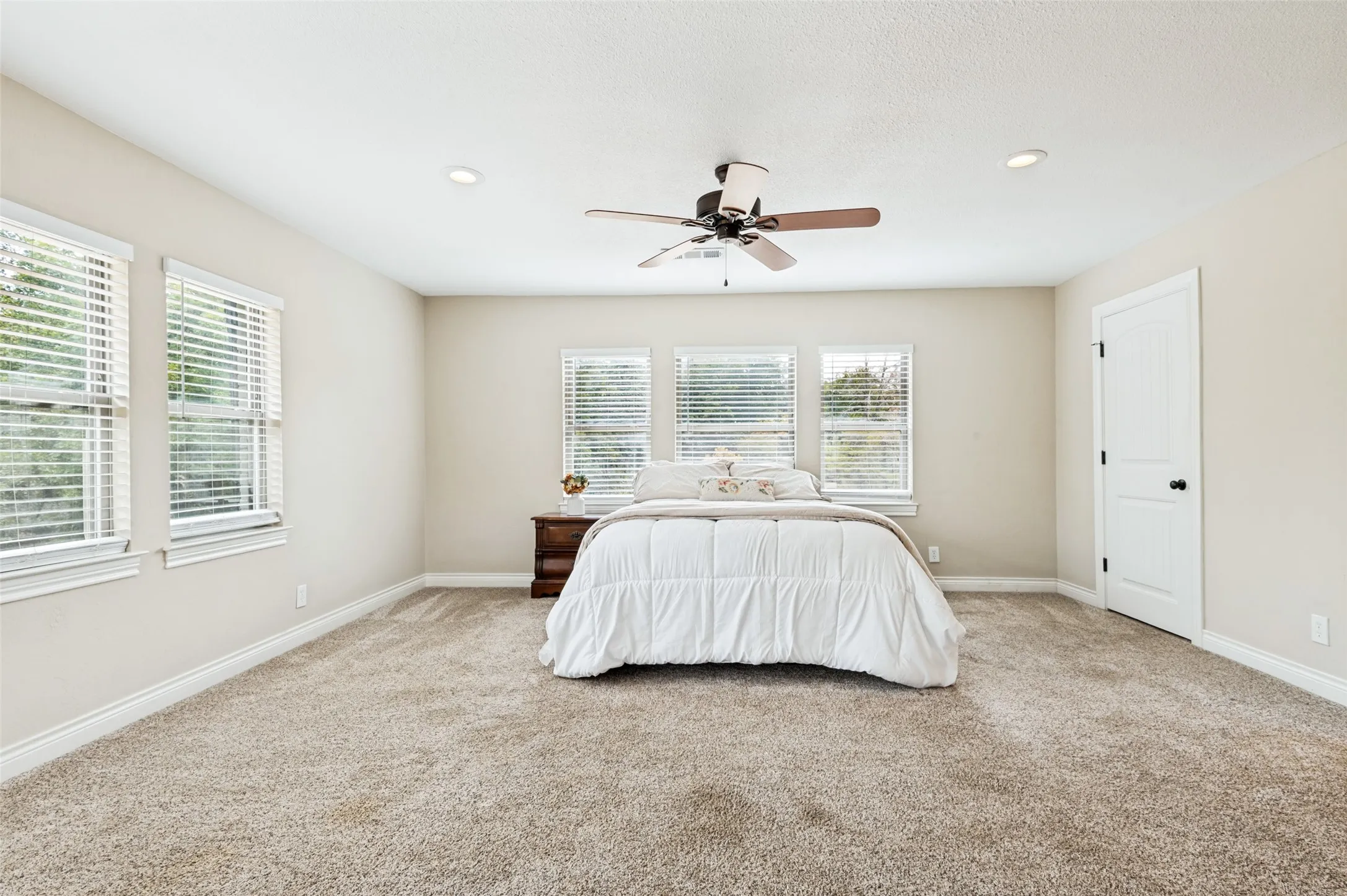 Plush carpet flooring, multiple windows with blinds, a ceiling fan with integrated lighting, and recessed ceiling lights