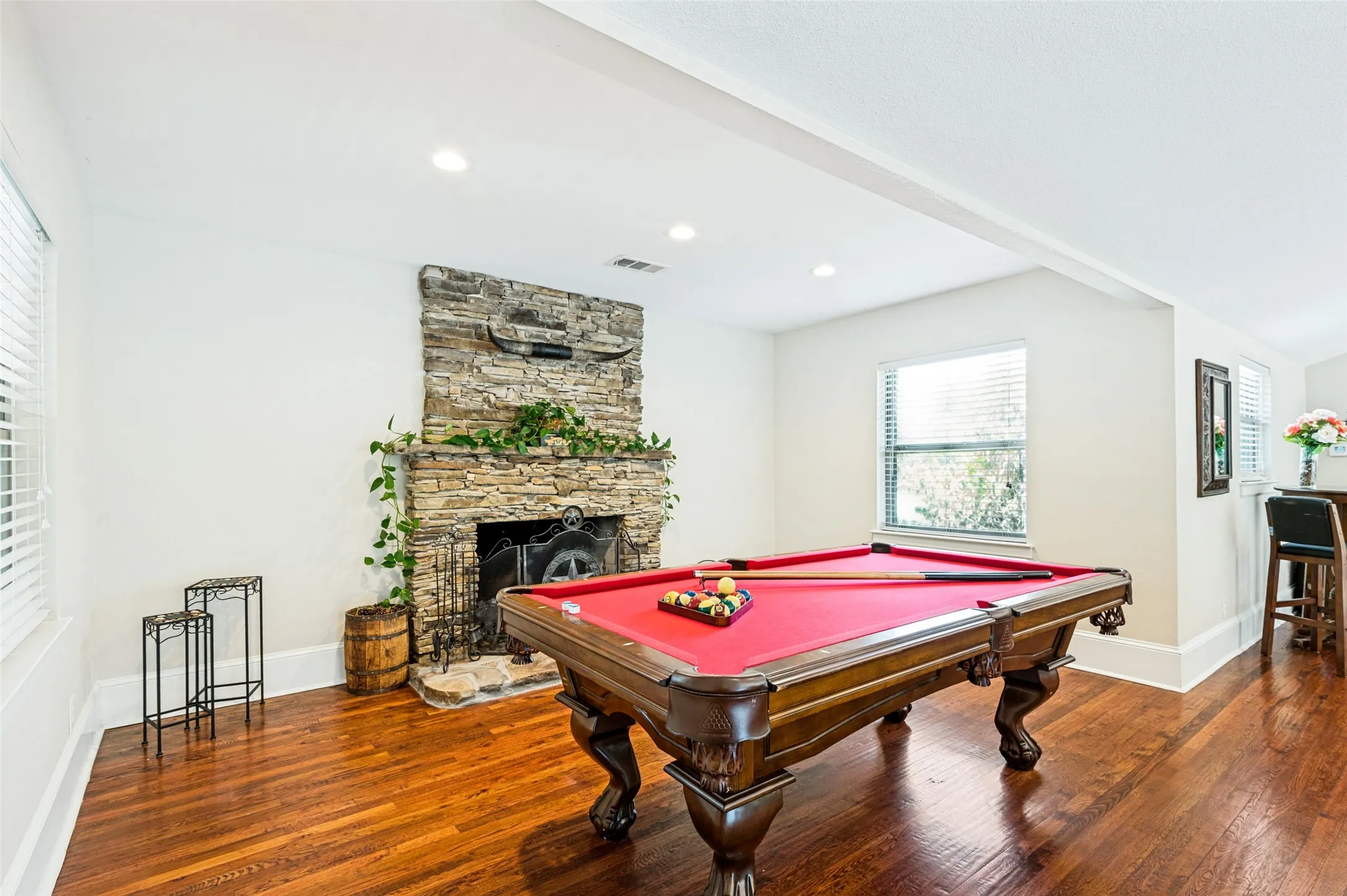 Stone-clad fireplace with hearth, recessed lighting, wood-finish flooring, and window with blinds