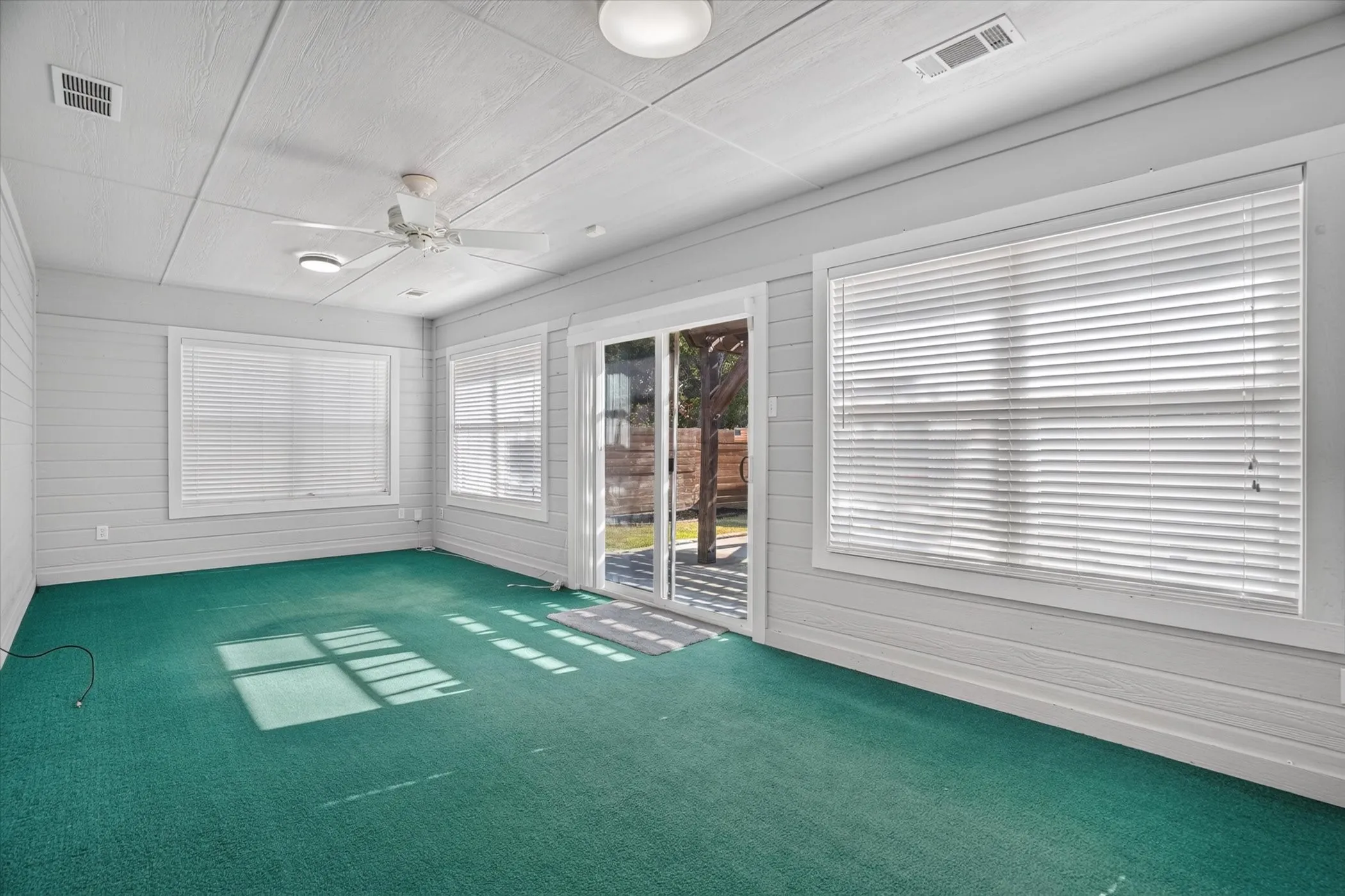 Room with shiplap walls, green carpeting, a ceiling fan, and multiple windows with blinds