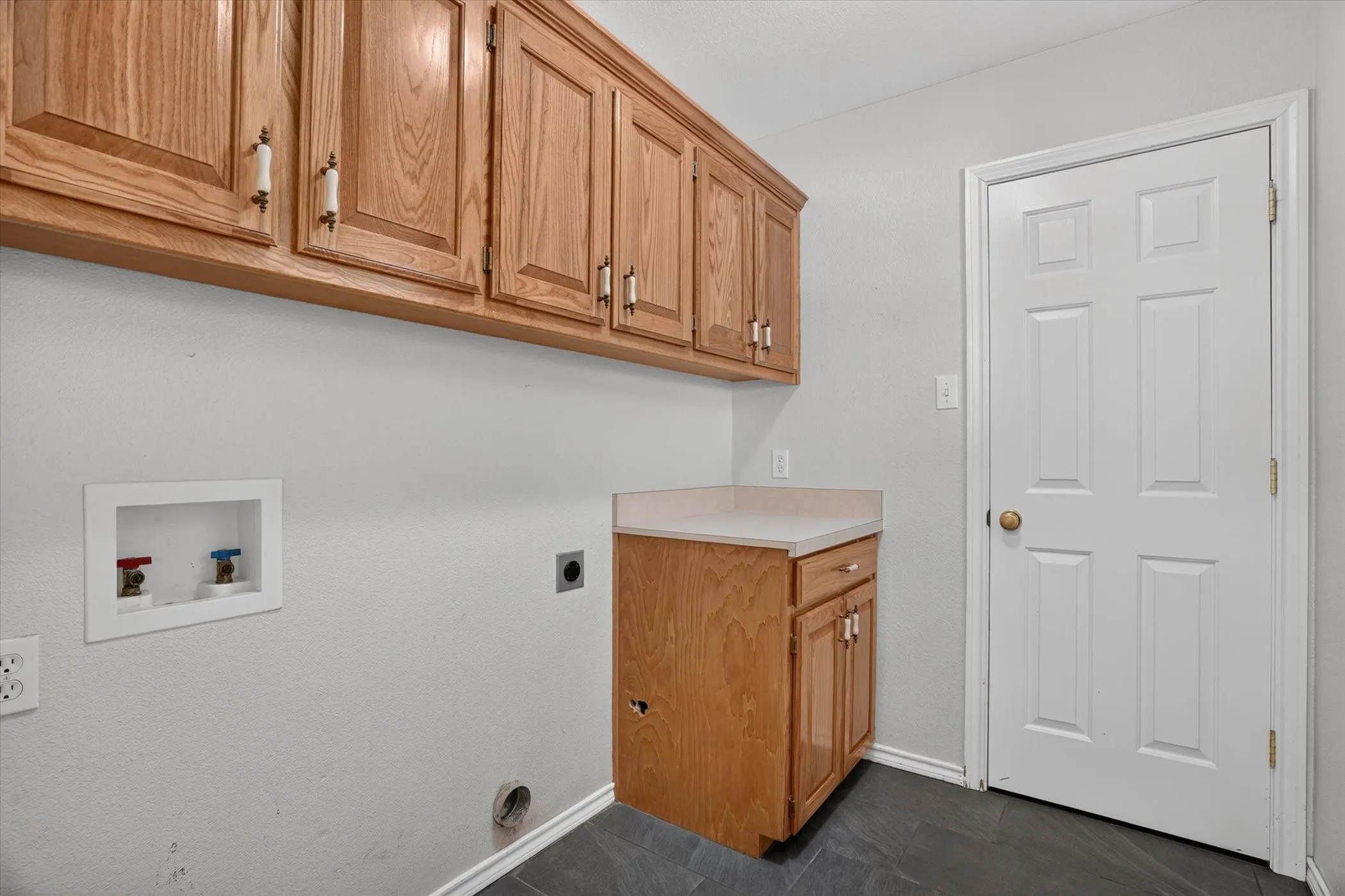 Wood-finish cabinetry, countertop space, and dark tile flooring