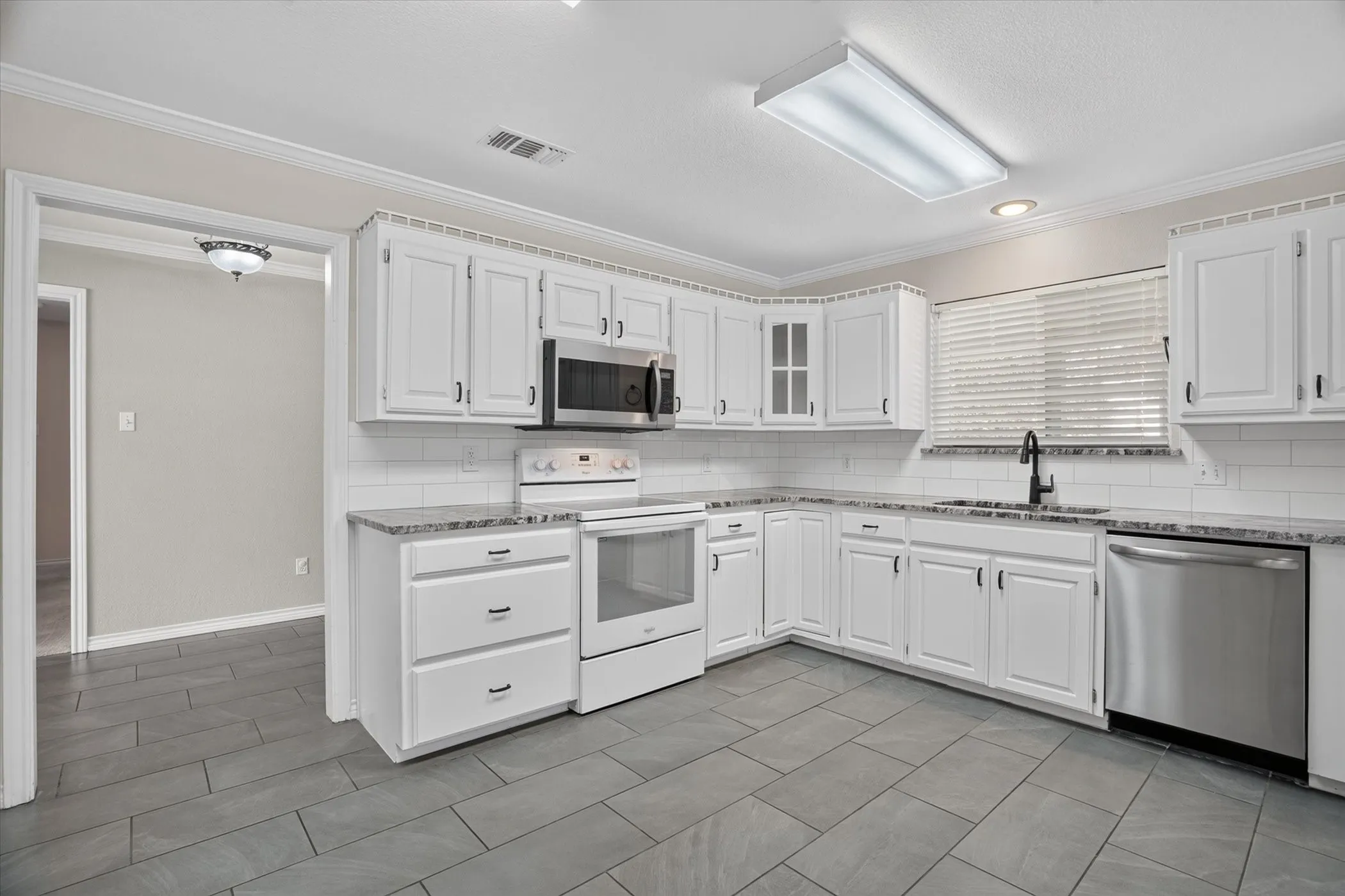 White cabinetry, subway tile backsplash, stainless steel appliances, dark countertop, and tiled flooring