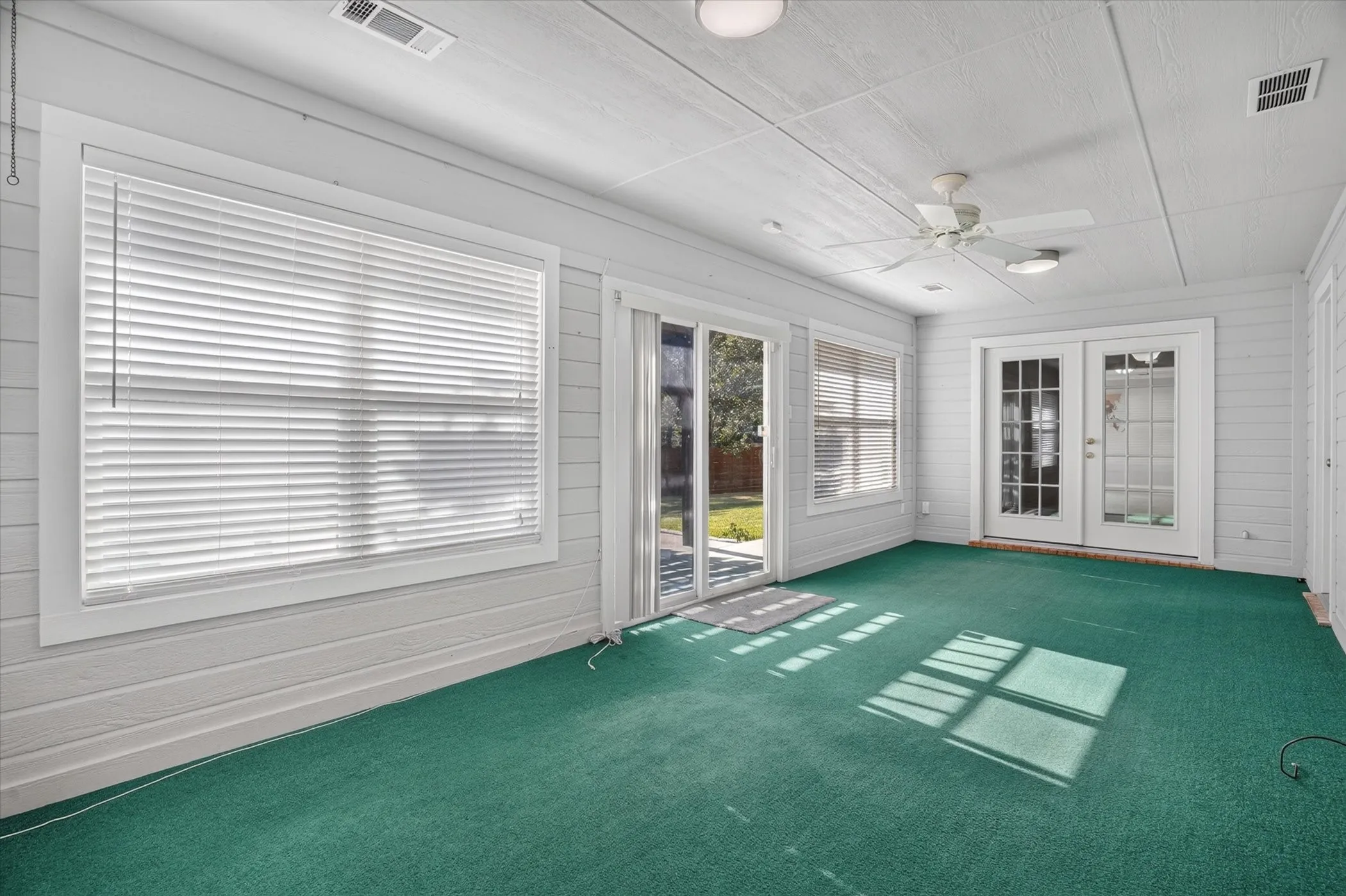 Carpeted sunroom featuring multiple windows with blinds, dual-pane sliding glass door, double French doors with glass panels, and a ceiling fan with integrated lighting