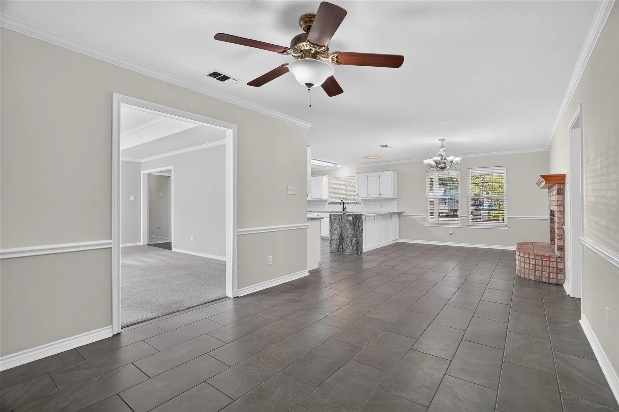 Spacious open-concept living area featuring large format tile flooring, crown molding, and a corner brick fireplace