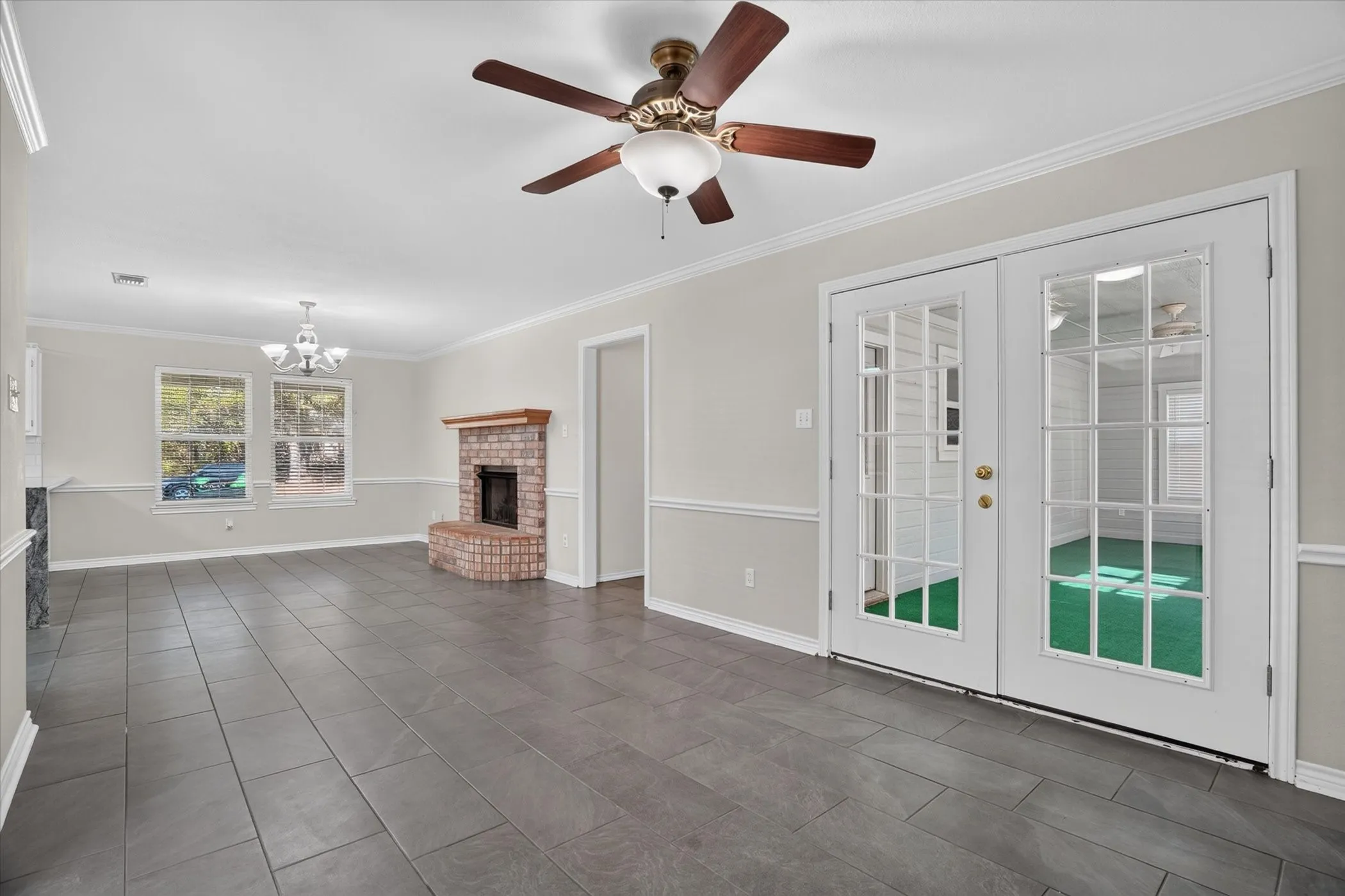 Rectangular tile flooring, a brick fireplace with a wood mantel, crown molding, and double glass-paneled doors