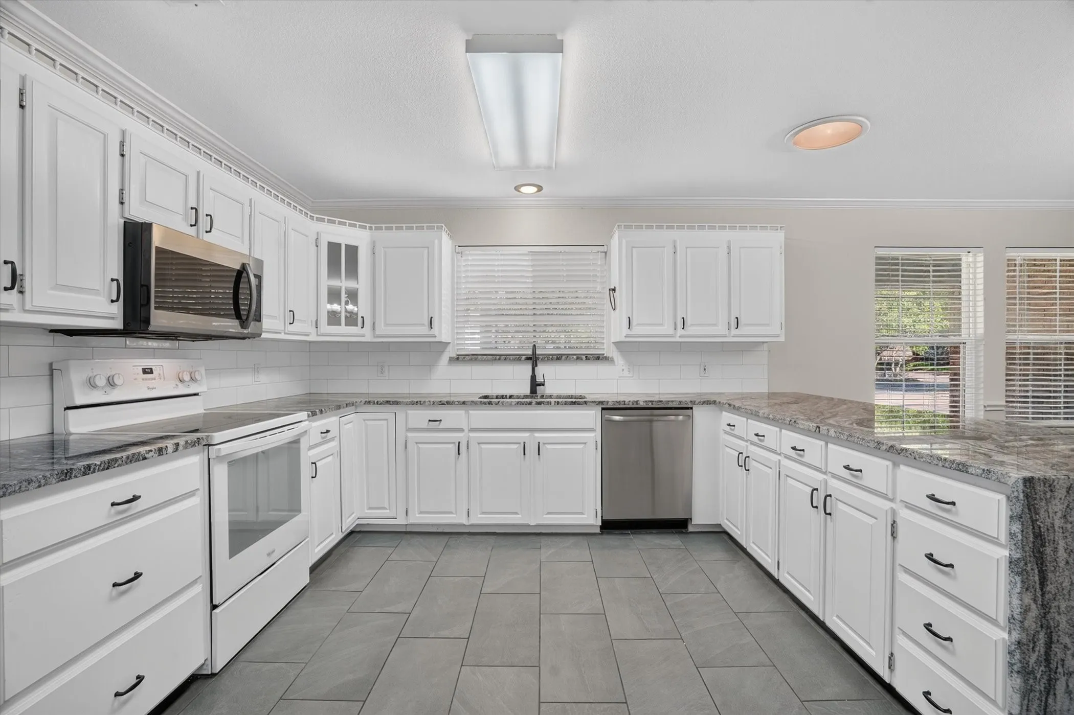Kitchen featuring white cabinetry, stone countertops, stainless steel appliances, subway tile backsplash, and tile flooring