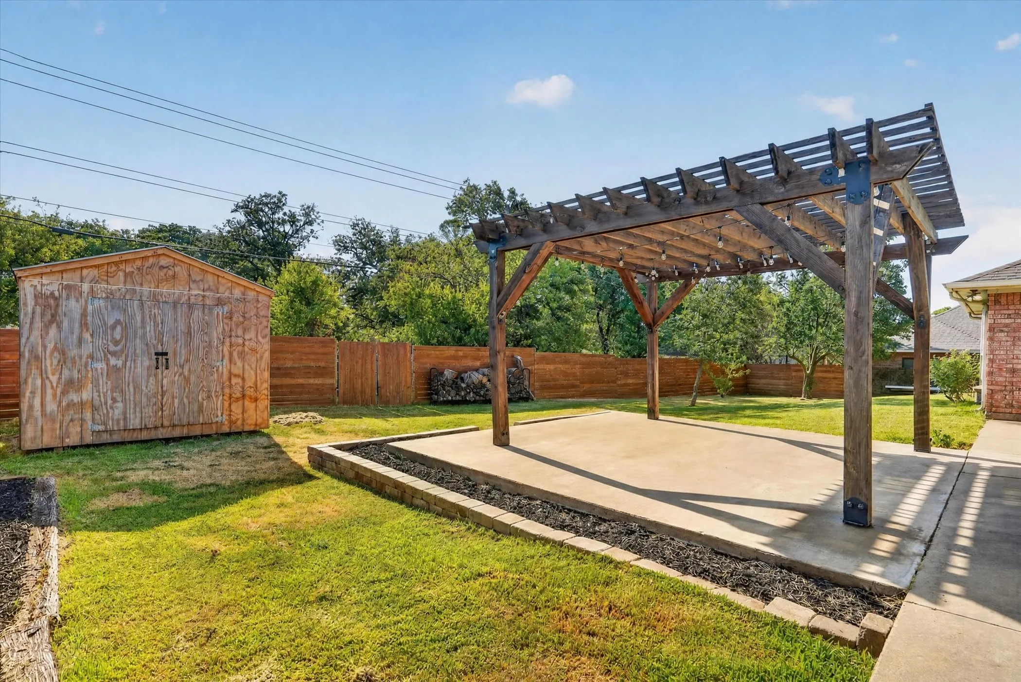 Spacious backyard oasis featuring a substantial wood-beam pergola with slatted roof panels casting dappled shade across a concrete patio