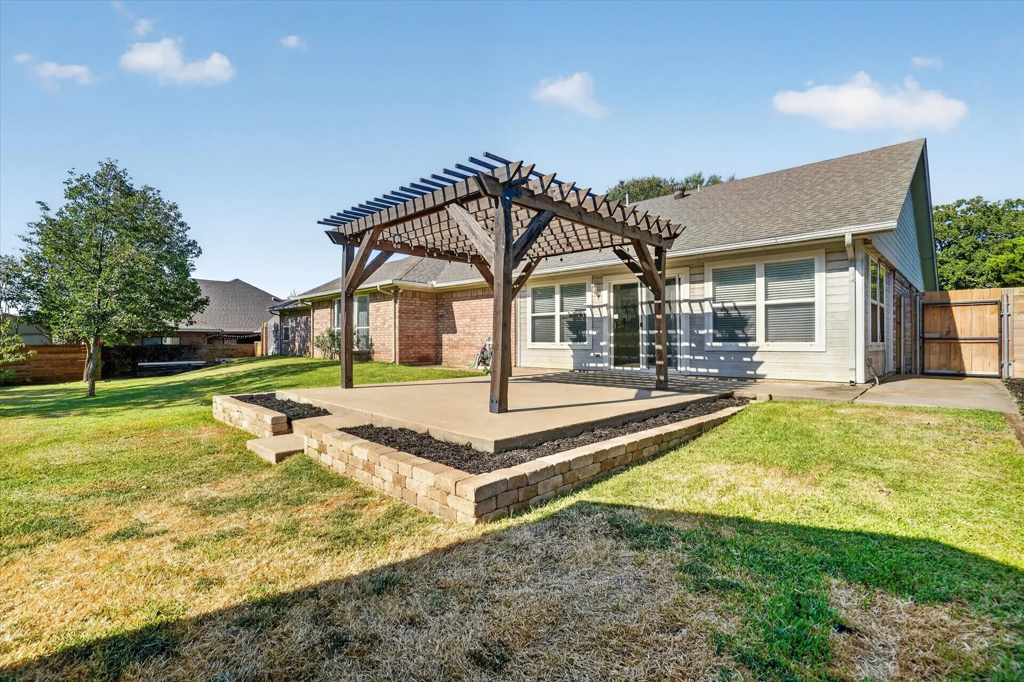 Backyard patio featuring a wooden pergola, concrete surfacing, and brick retaining walls