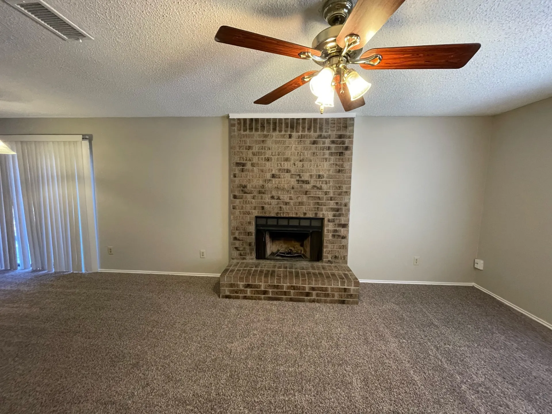 Unfurnished living room with a textured ceiling, carpet floors, a fireplace, and ceiling fan