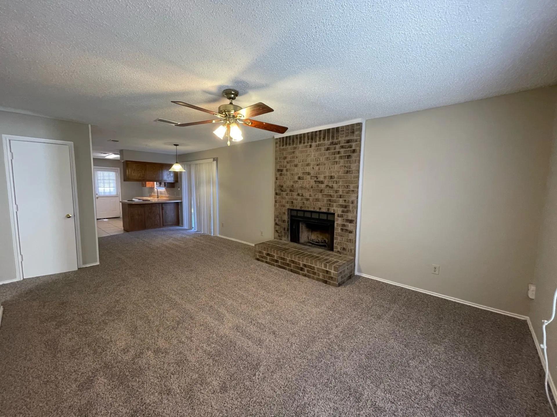 Unfurnished living room featuring carpet, a textured ceiling, a fireplace, and a ceiling fan