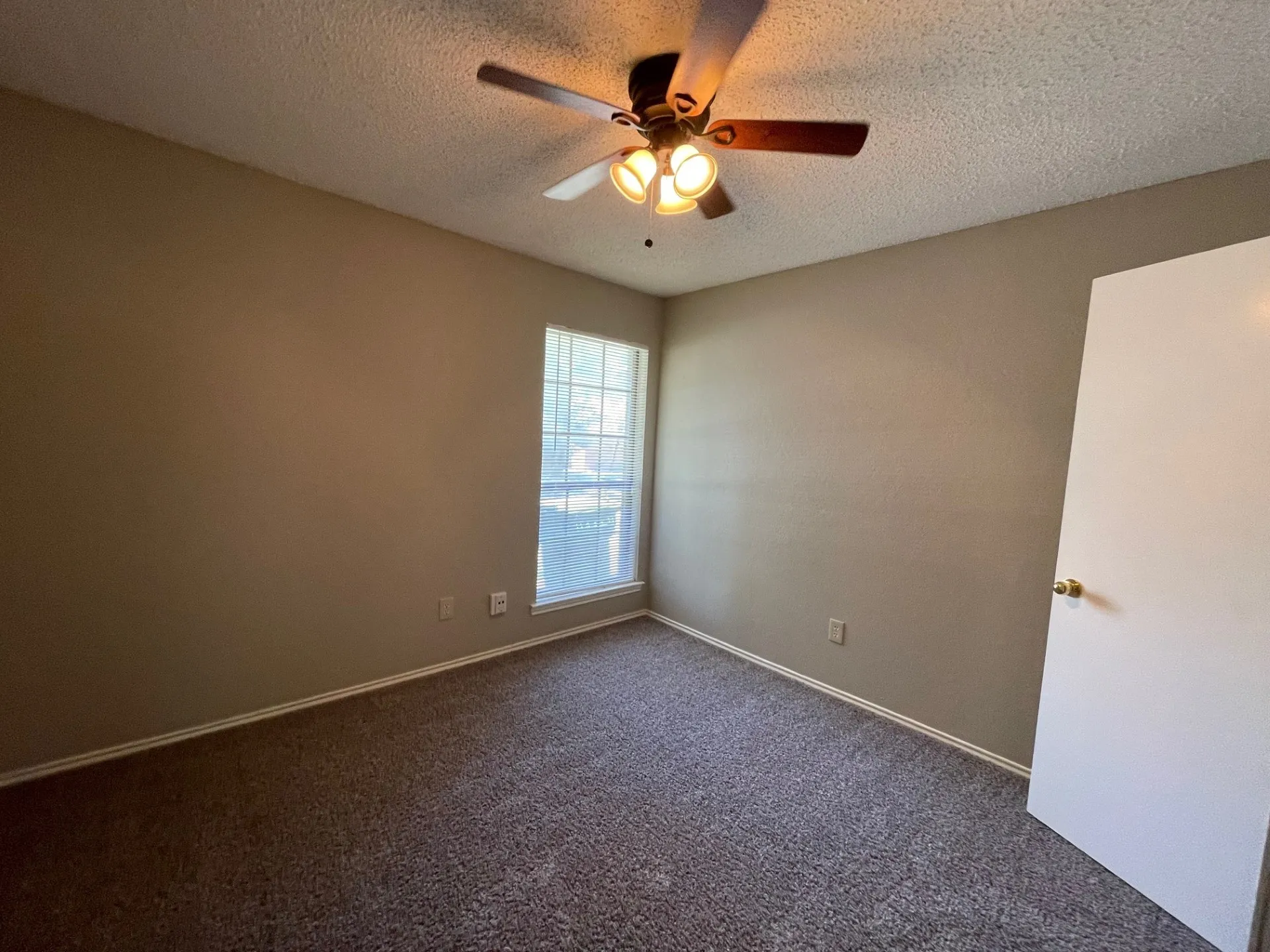 Empty room with a textured ceiling, dark colored carpet, and a ceiling fan