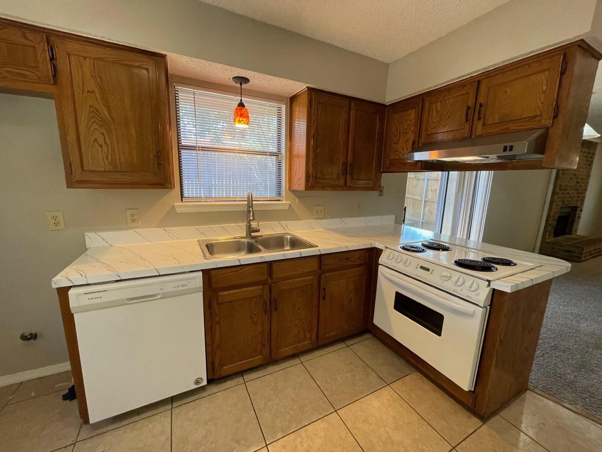 Kitchen with white appliances, a textured ceiling, a peninsula, under cabinet range hood, and light tile patterned floors