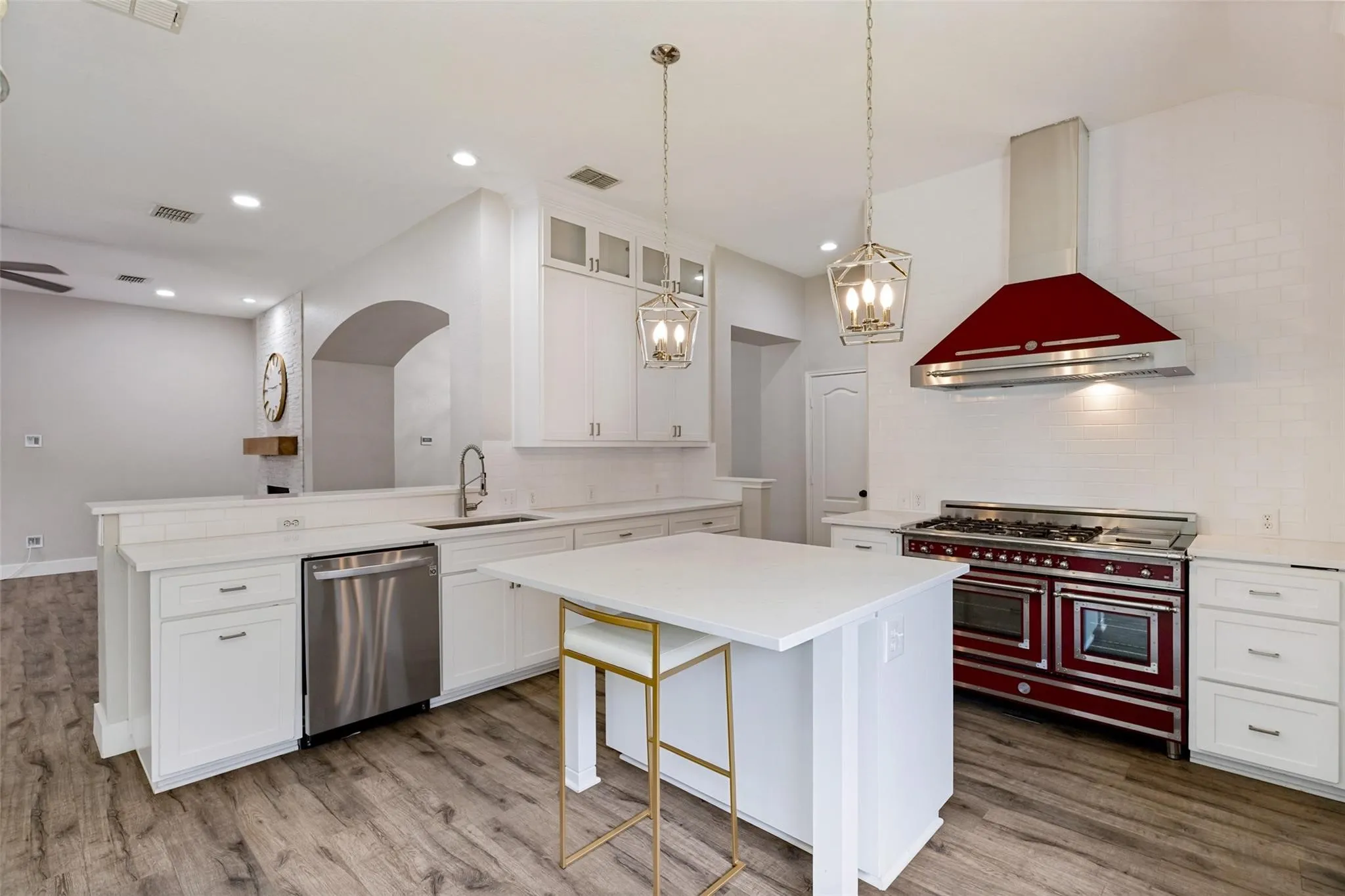 Gourmet kitchen with white cabinetry, a central island, stainless steel appliances including a striking red range, and wood-finish flooring