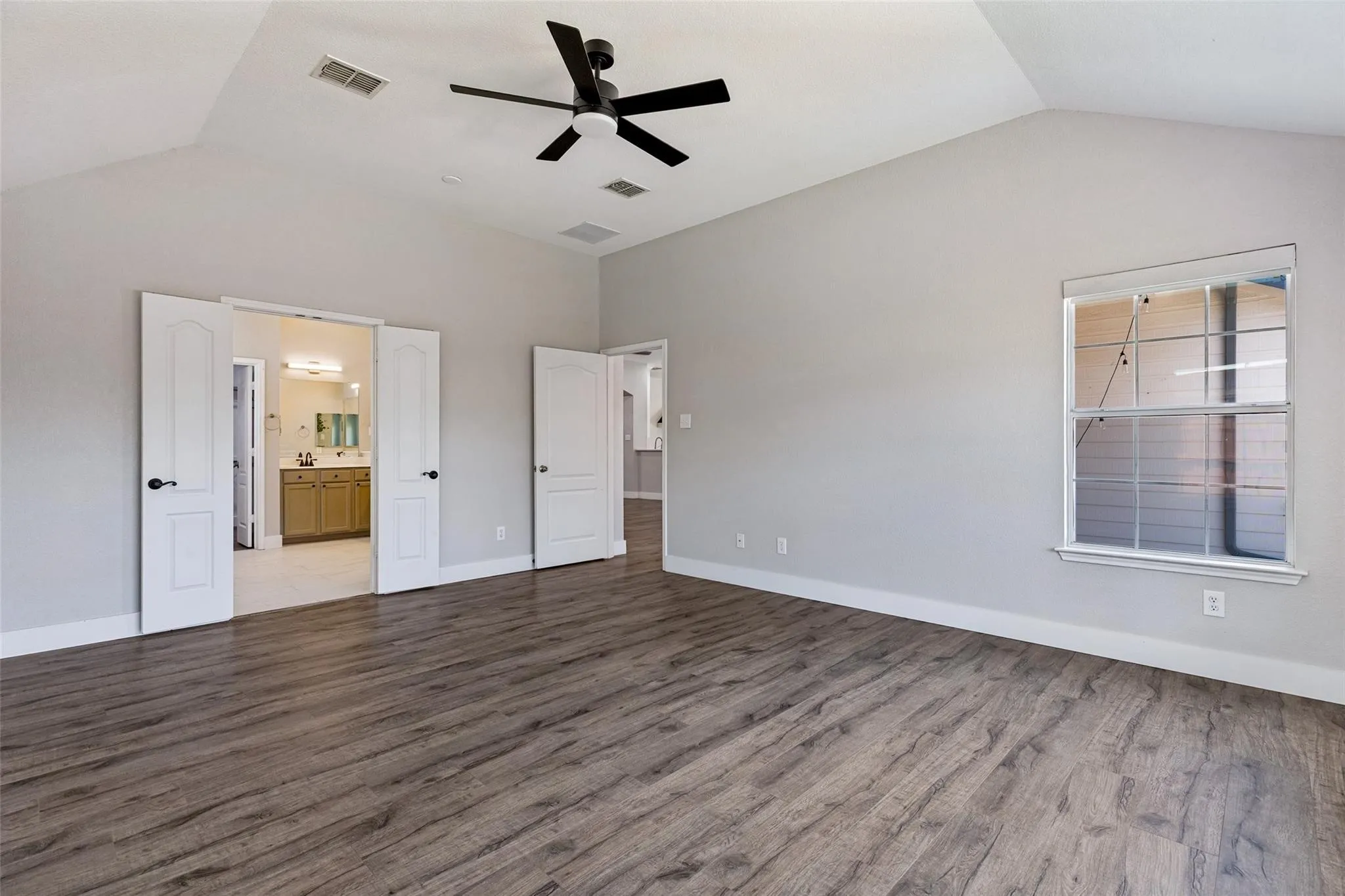 Vaulted ceiling with a black ceiling fan, wood-finish flooring, and a single window