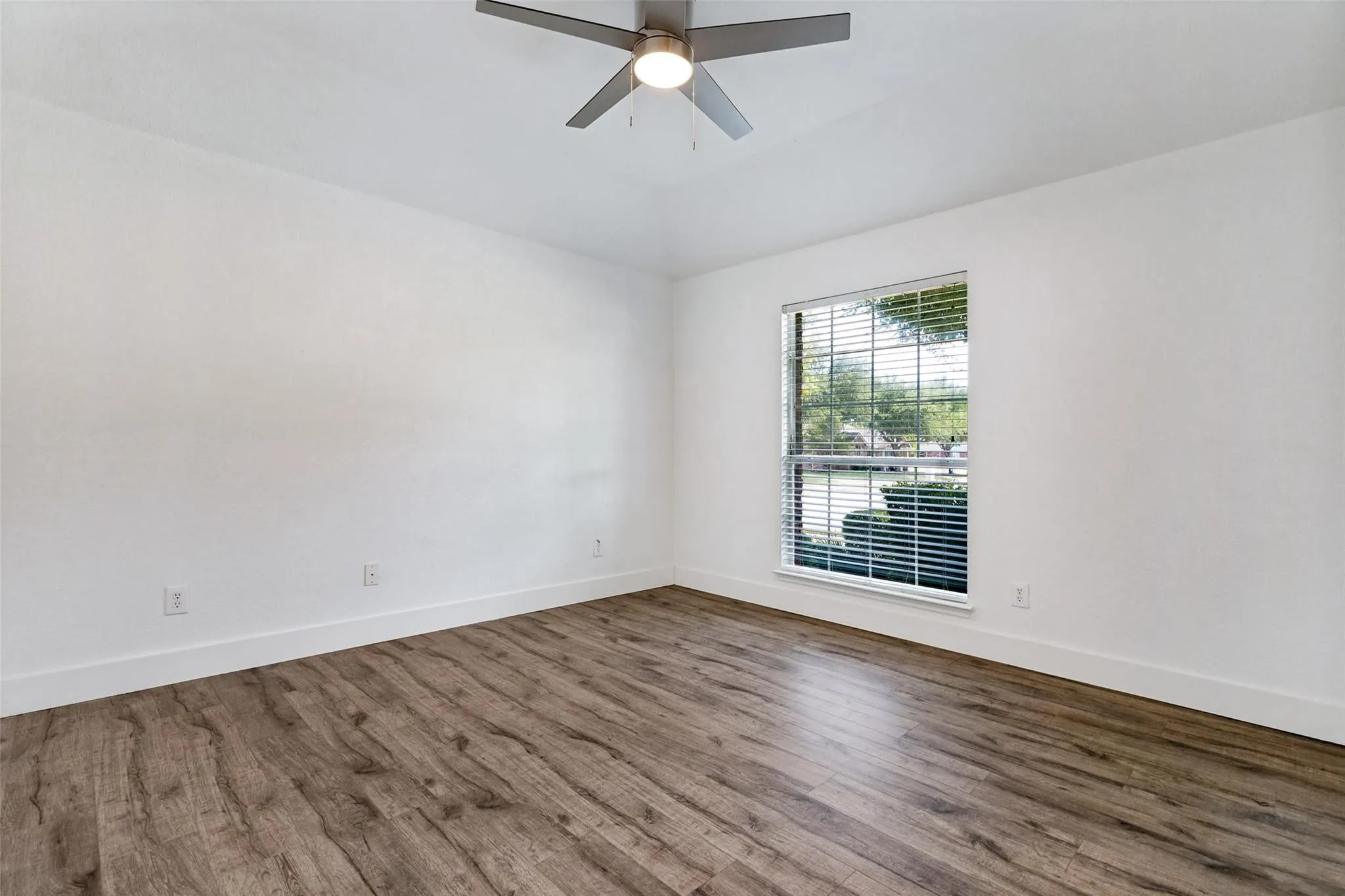 Wood-finish flooring, white walls, and a window with blinds