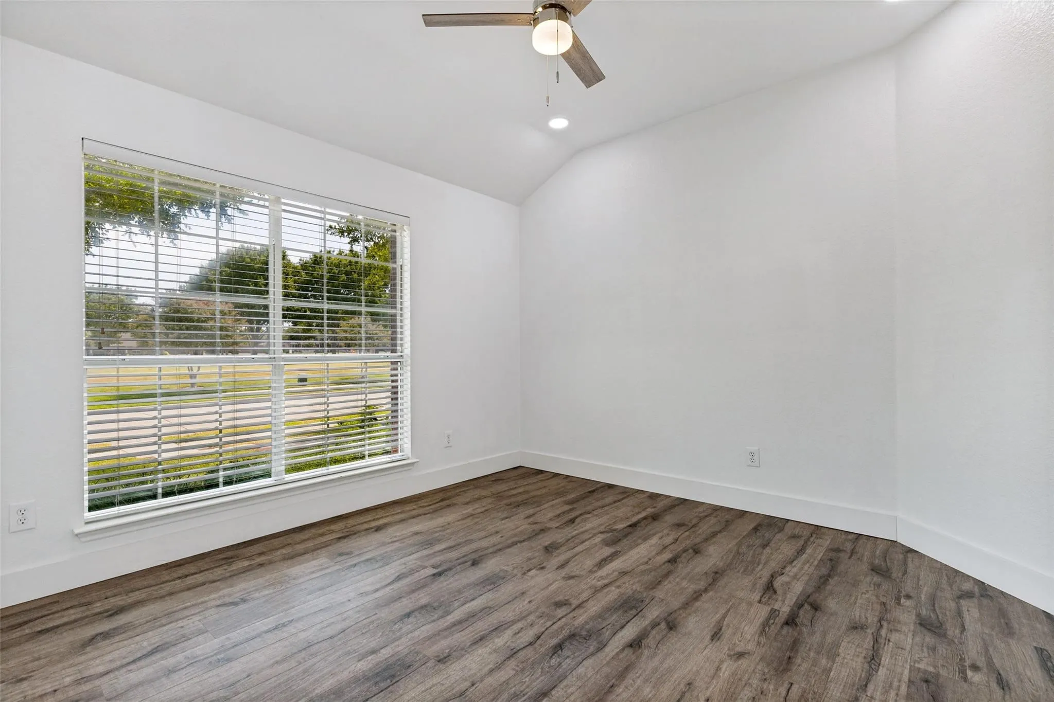 Spacious room featuring wood-finish flooring, a large window with blinds, a ceiling fan, and recessed lighting