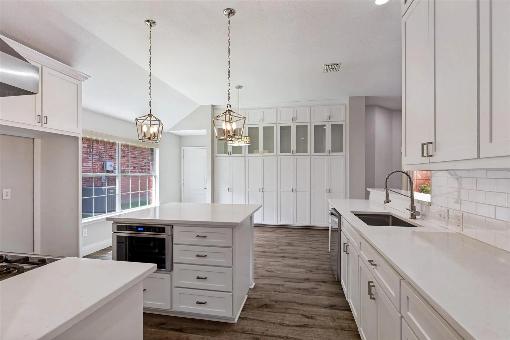 Kitchen featuring white cabinetry, wood-finish flooring, a central island with built-in microwave, white countertops, and subway tile backsplash