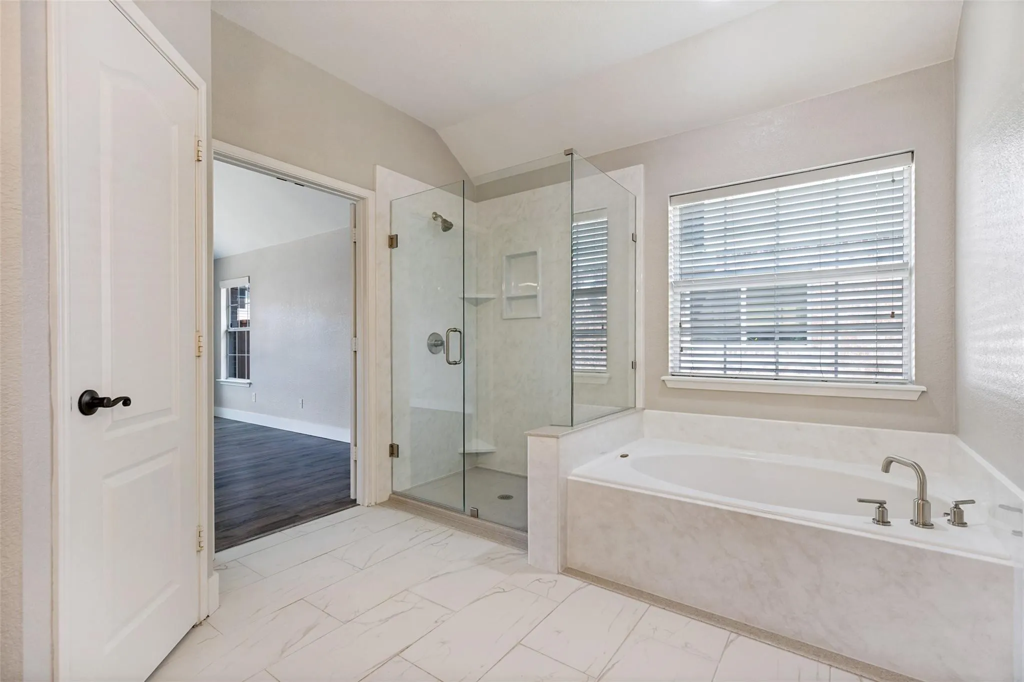 Walk-in glass shower, built-in bathtub with deck-mounted fixtures, and large window with blinds