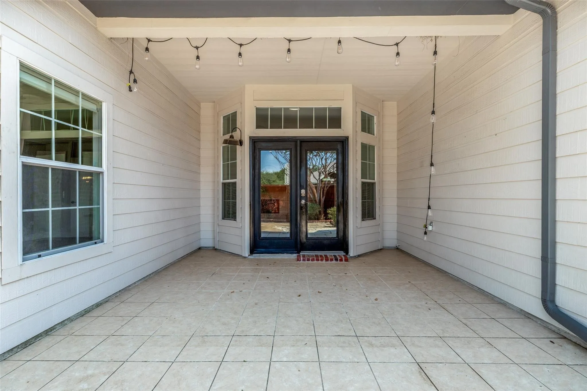 Covered patio featuring tiled flooring, a double glass-panel door entry, and two side windows with transom accents