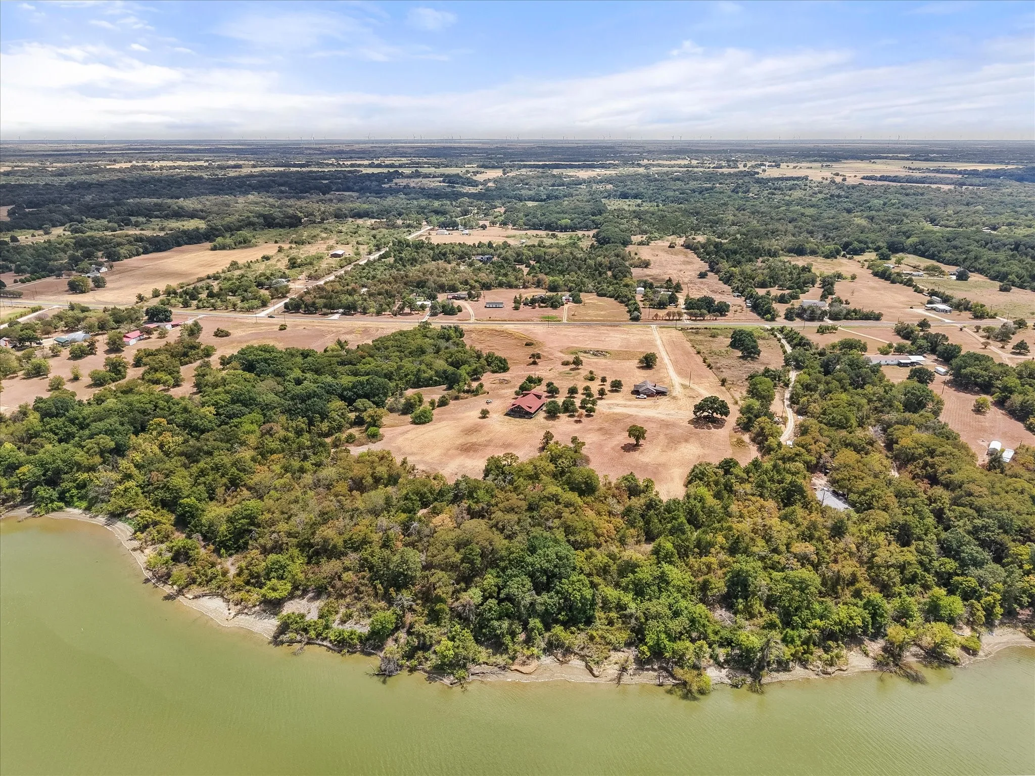 Waterfront property featuring a wooded shoreline, expansive clearings, and mature trees