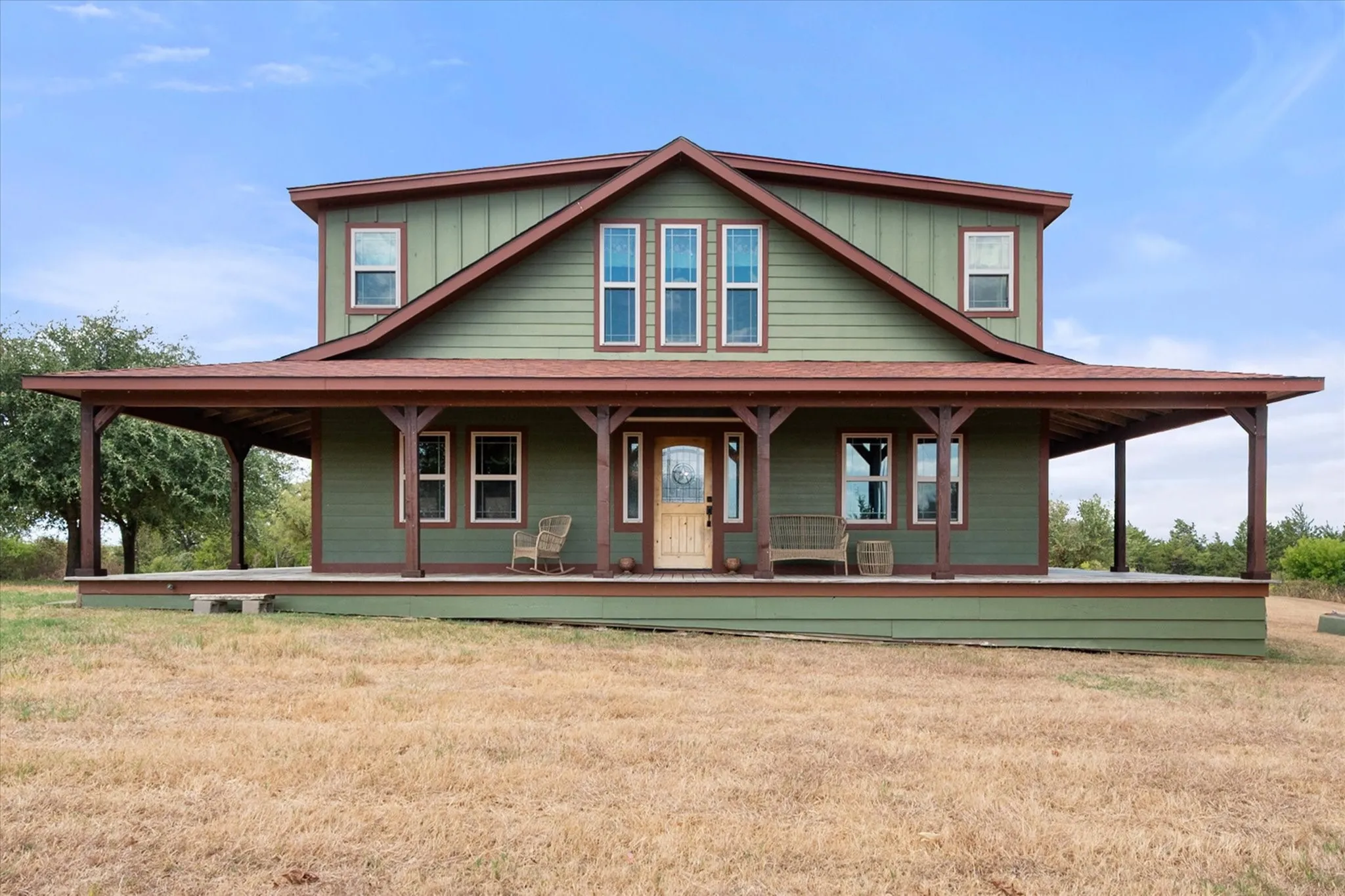 Two-story home with a full-length covered porch, green siding, and a prominent front gable