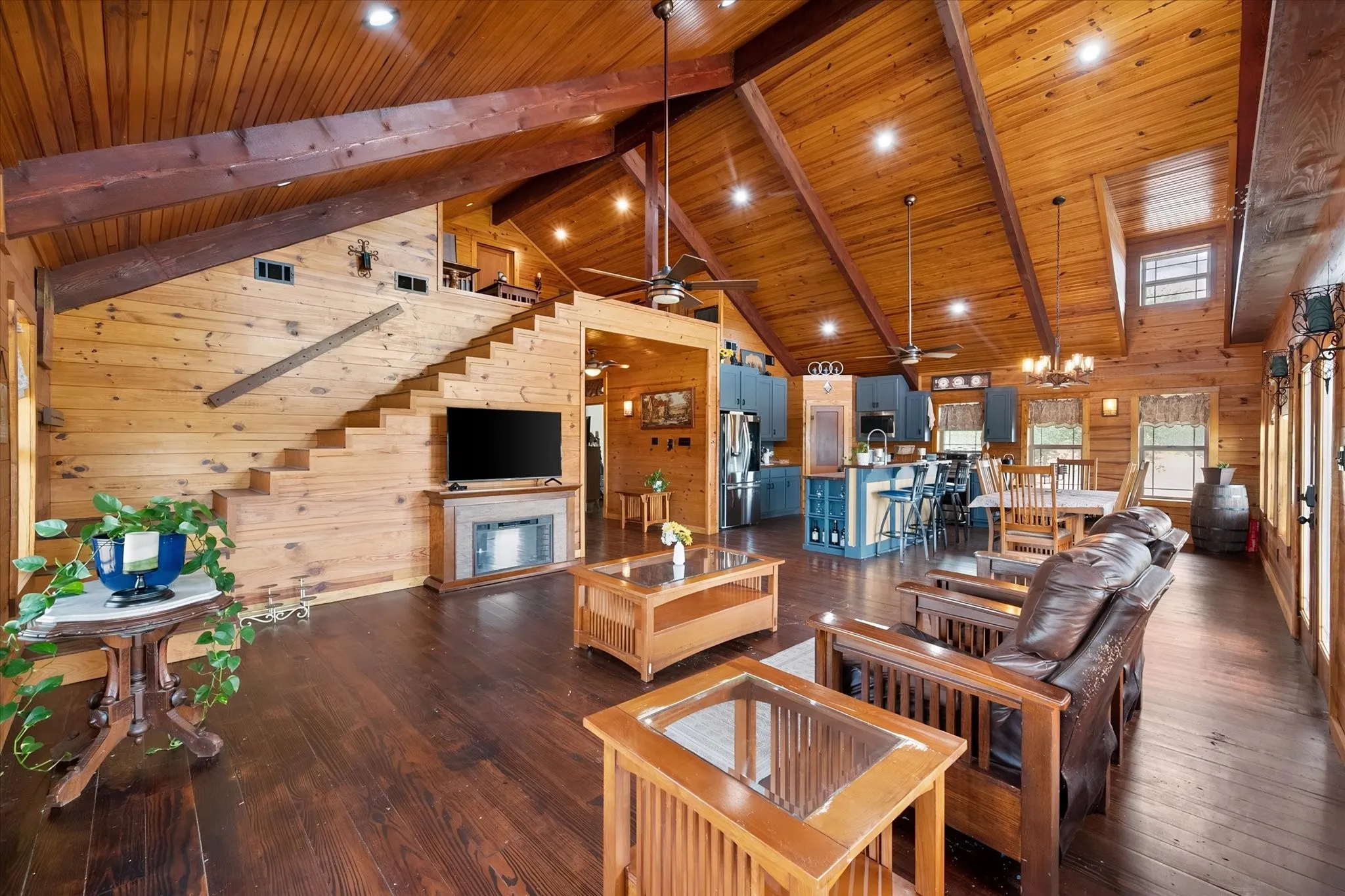 Vaulted wood-paneled ceilings with exposed beams, wood-finish flooring, a built-in fireplace, a wood staircase, and a kitchen with blue cabinetry