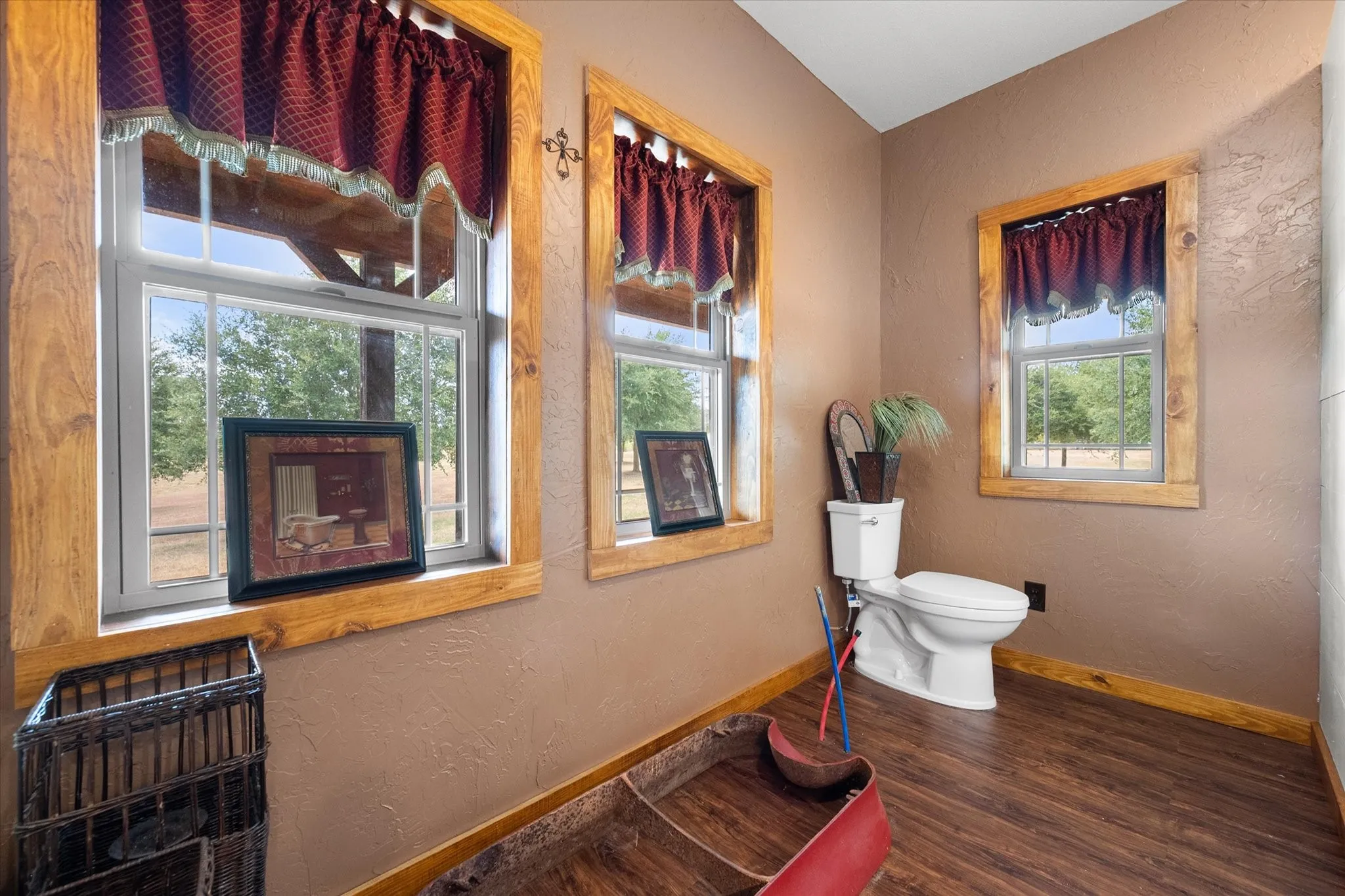 Wood-finish flooring, multiple windows with natural wood trim, and a white toilet