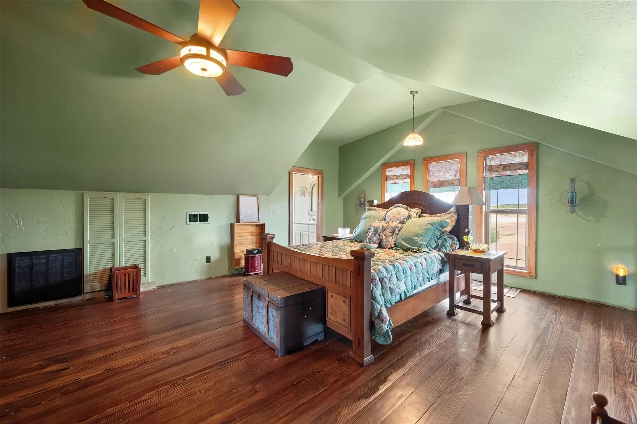 Primary Bedroom with vaulted ceilings, wood-finish flooring, three windows with wood trim, built-in wall paneling, and a ceiling fan with integrated lighting
