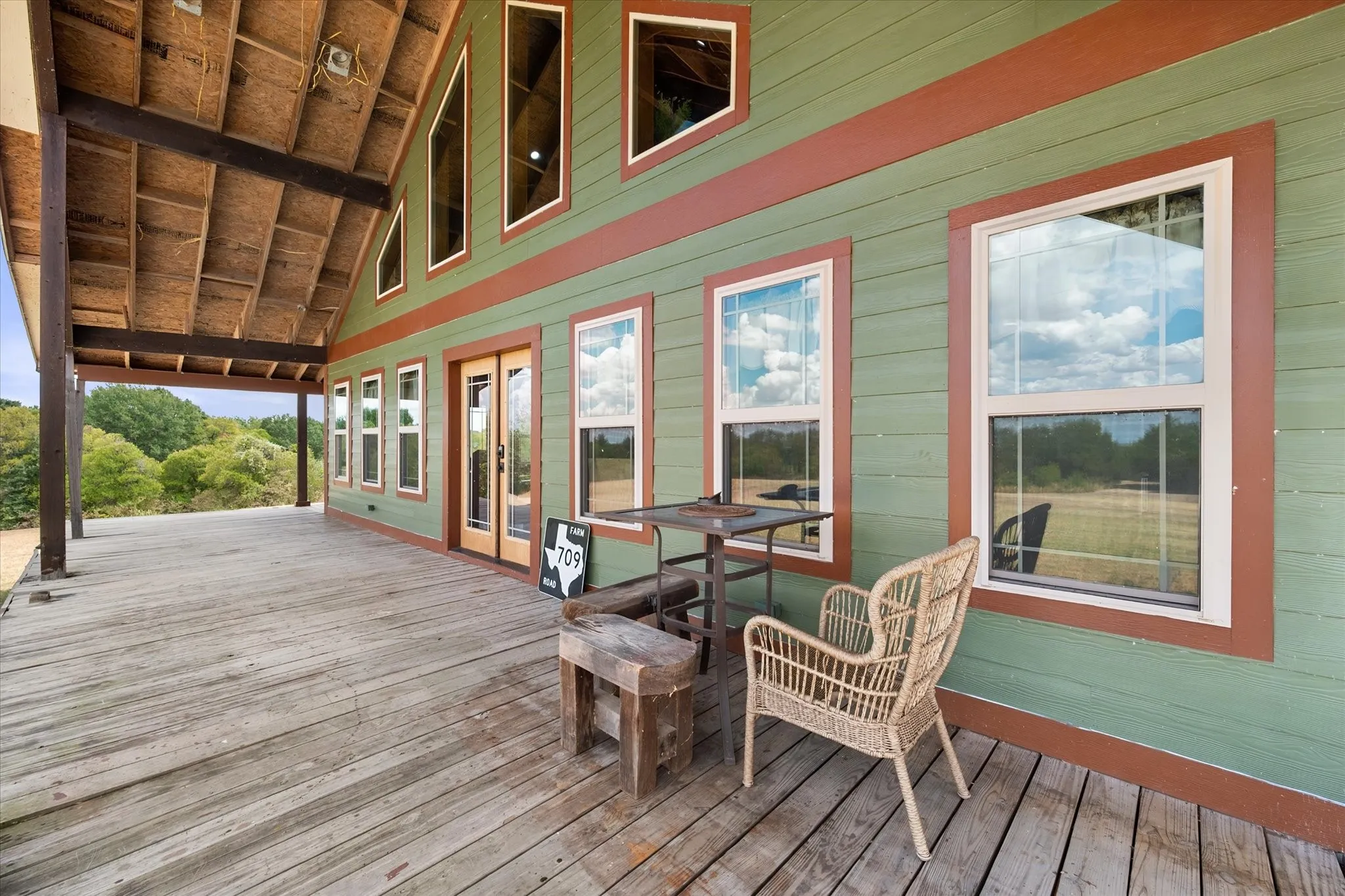 Expansive covered wood-deck porch with exposed beam ceiling, multiple windows, and a double-door entry