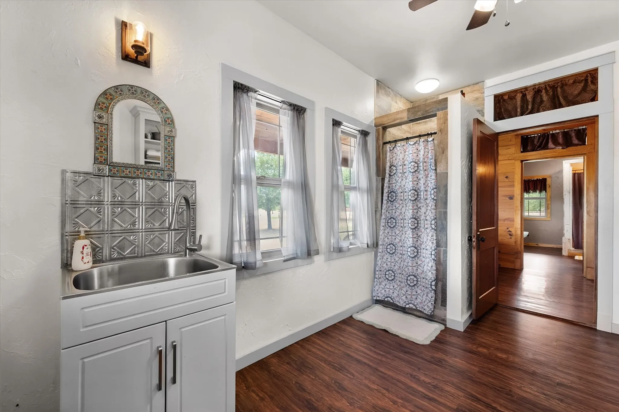 Wood-finish flooring, built-in utility sink with metal backsplash, wood-paneled shower enclosure, and a ceiling fan