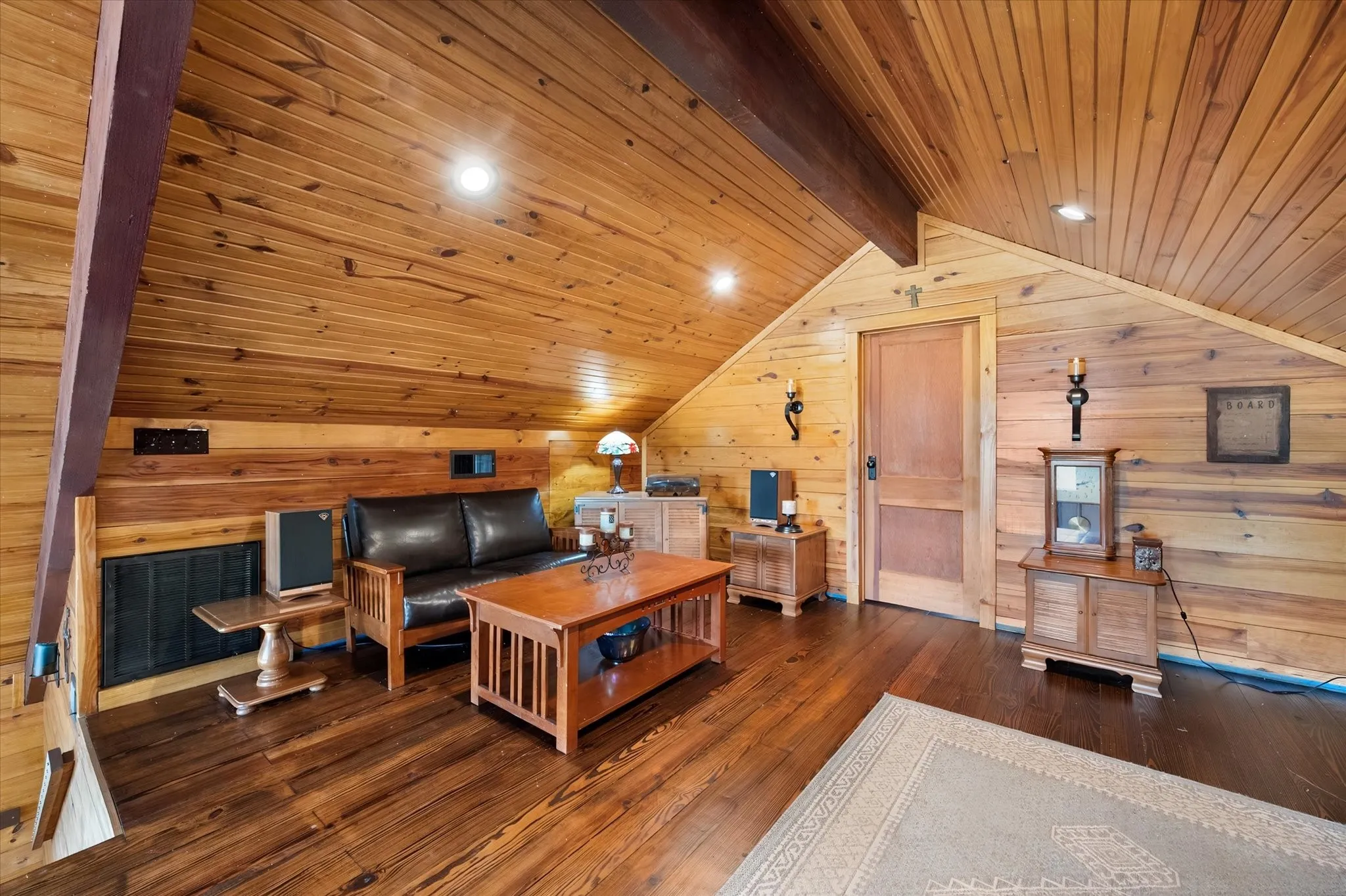 Wood-paneled walls and ceiling, exposed structural beam, wood-finish flooring, recessed lighting, and wall-mounted sconces
