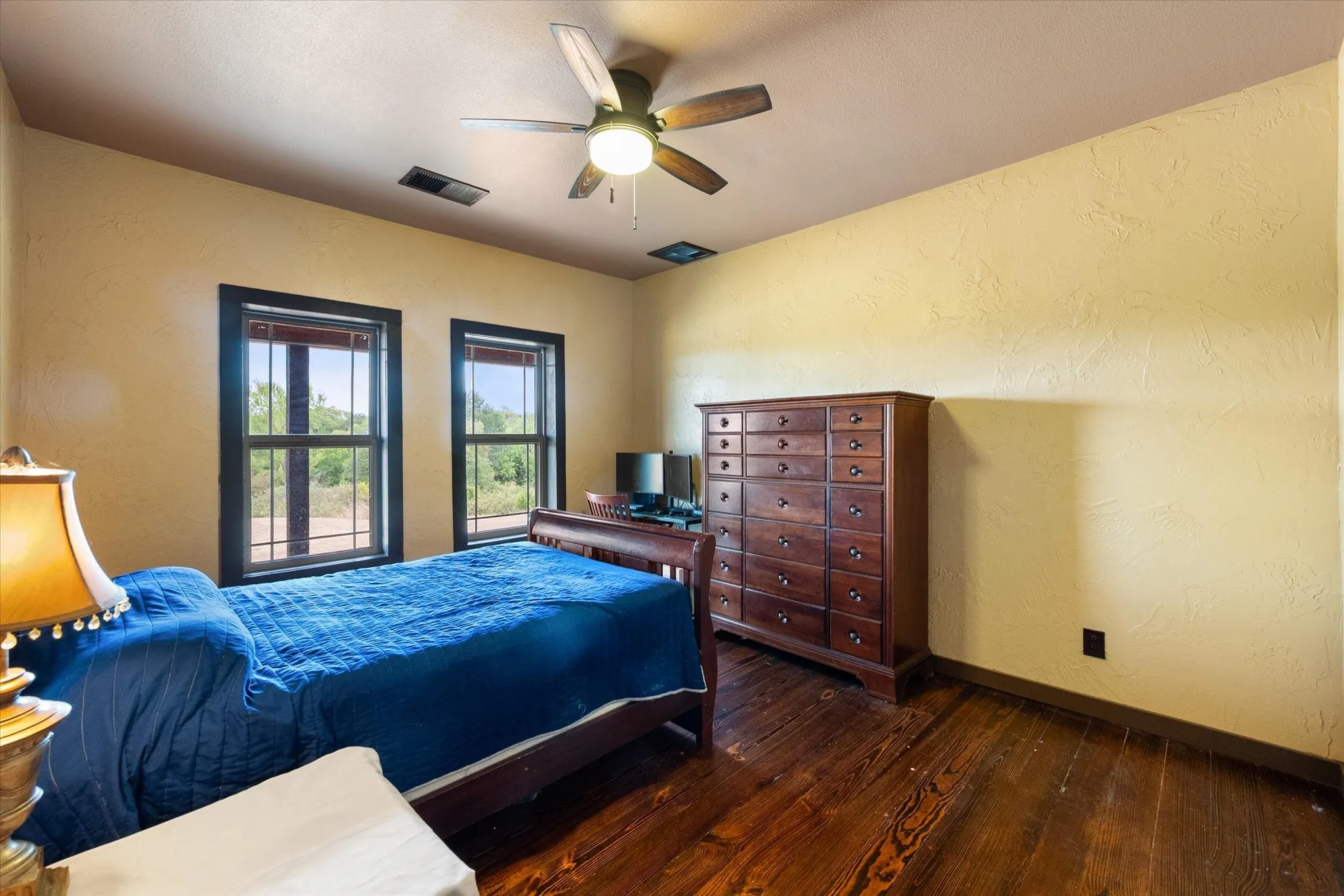 Hardwood flooring, textured walls, dual windows with dark trim, and a ceiling fan with integrated lighting