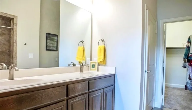 Primary bathroom showing dual sinks, door to toilet, and entry to walk-in closet