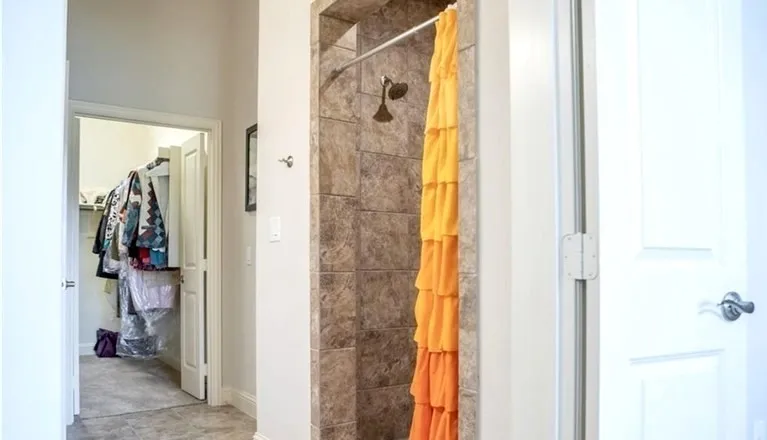Primary bathroom showing walk-in doorless stone shower and entry to closet