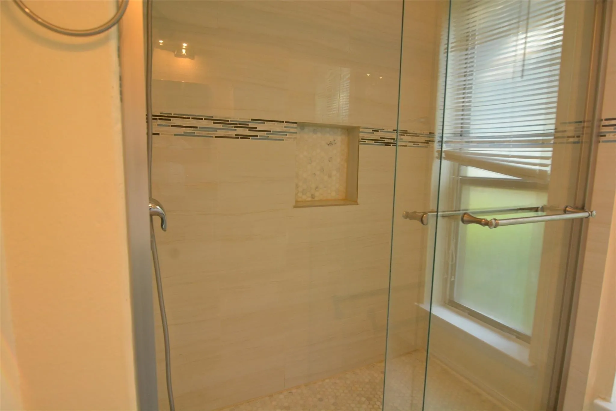 Glass-enclosed shower featuring a tiled surround, decorative mosaic accent, and a built-in shower niche