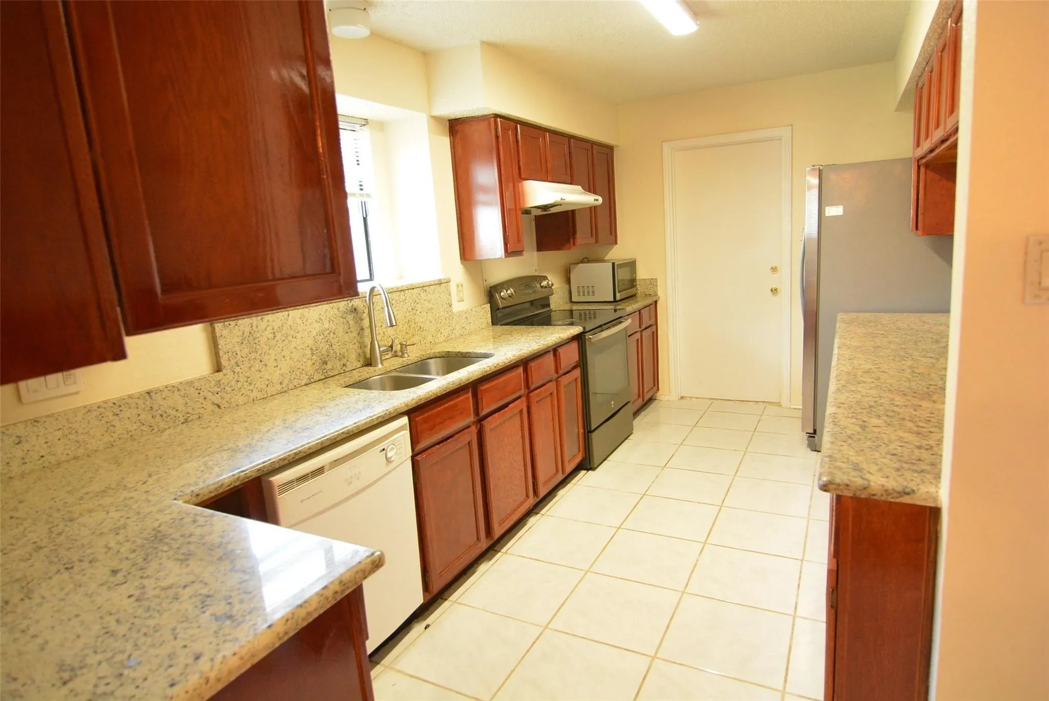 Kitchen featuring extensive wood cabinetry, light speckled countertops, stainless steel appliances, a double basin sink, and tile flooring