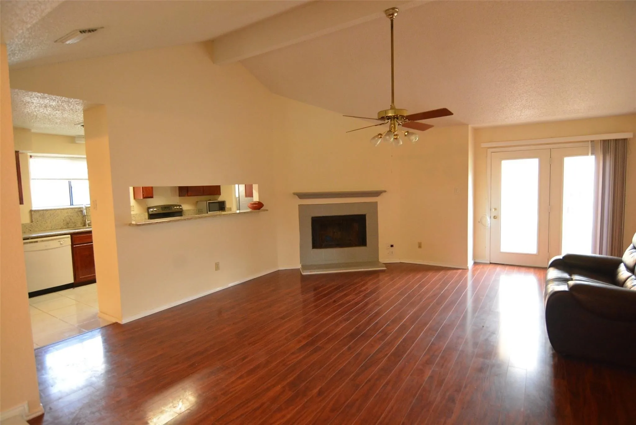 Spacious room featuring vaulted ceilings, wood-finish flooring, a fireplace with a stone surround, and double glass panel doors