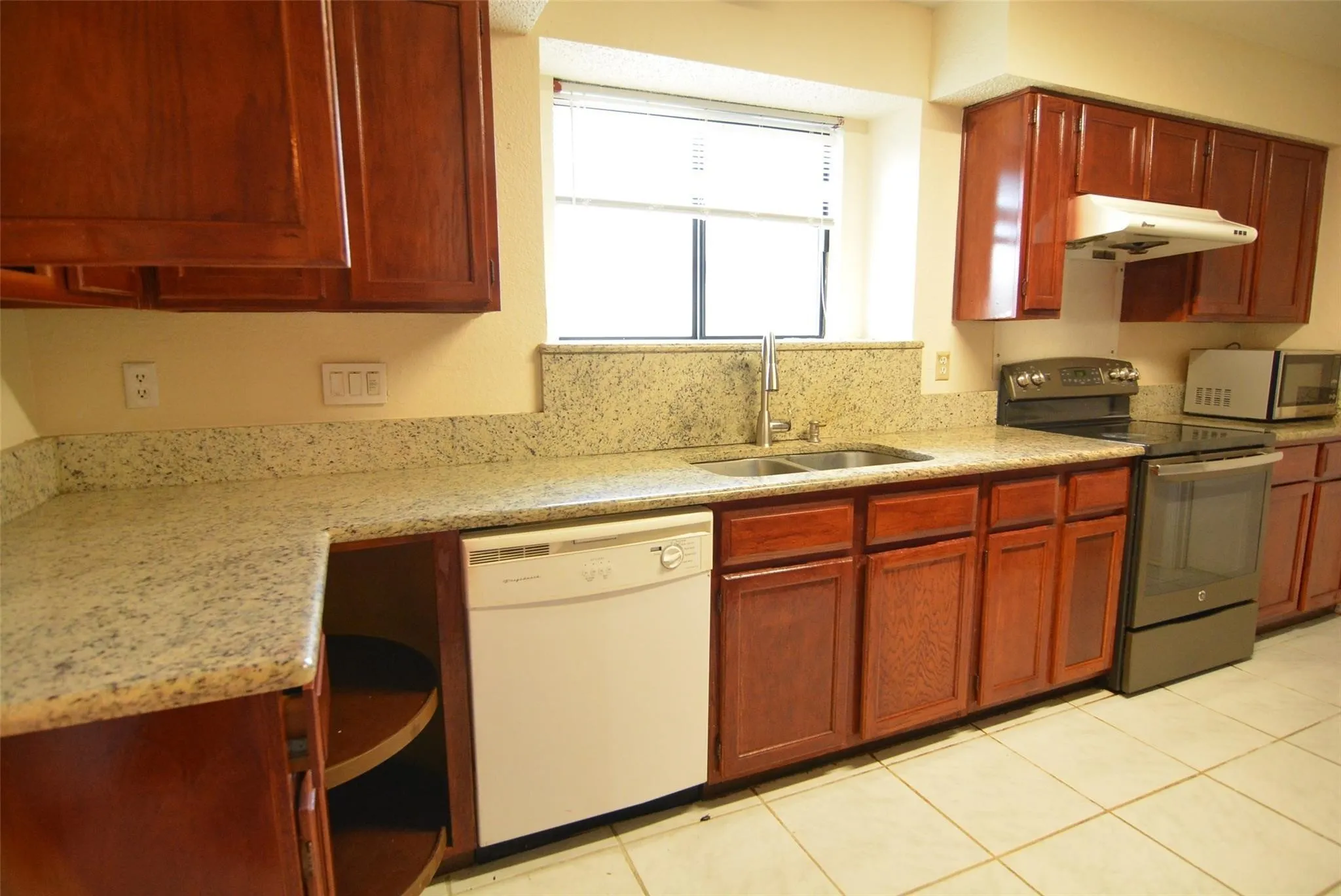 Kitchen with wood-finish cabinetry, light-toned countertops, tile flooring, and a stainless steel double-basin sink
